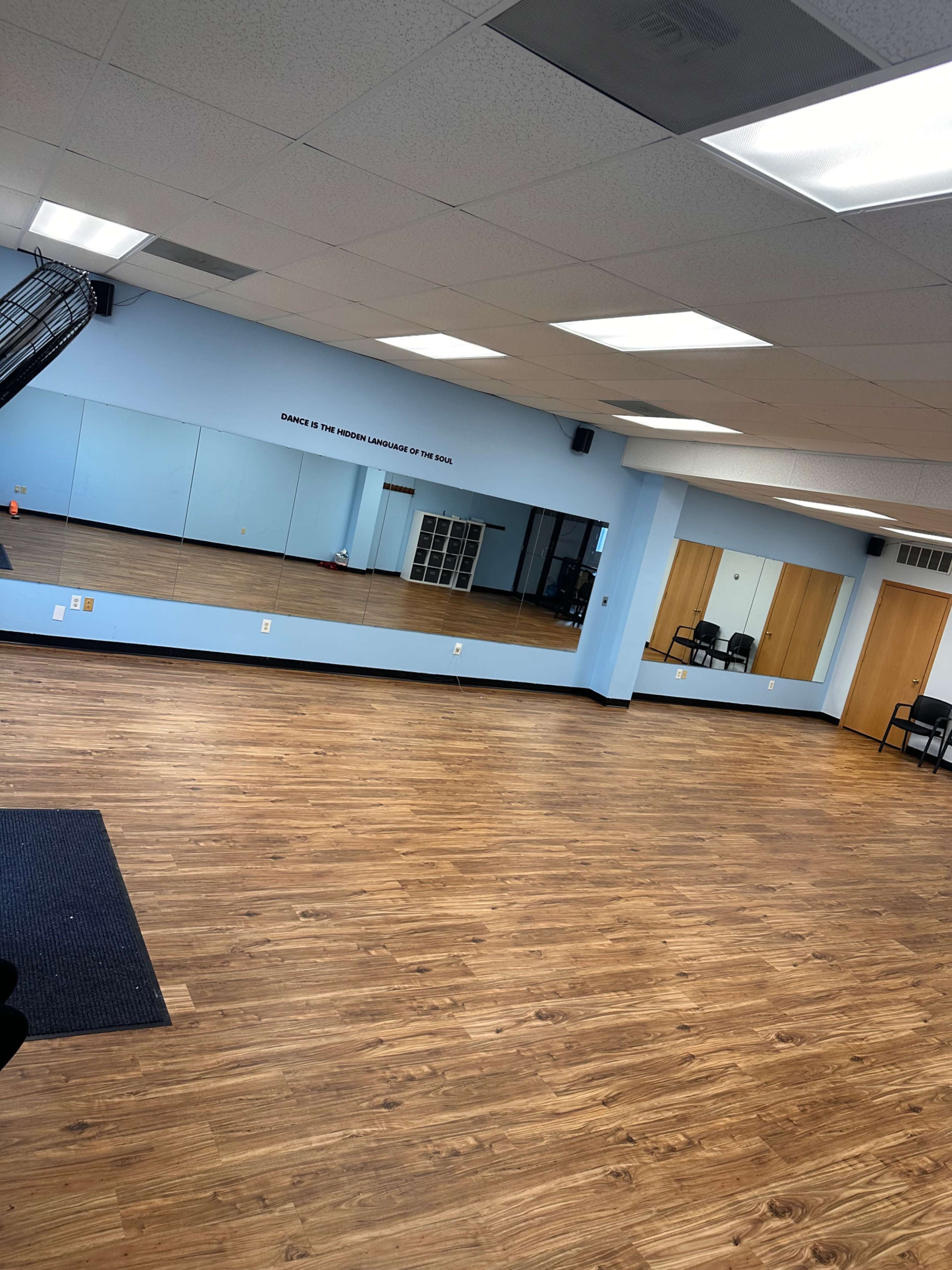 An empty room with wooden flooring, blue walls, and large mirrors along one side.