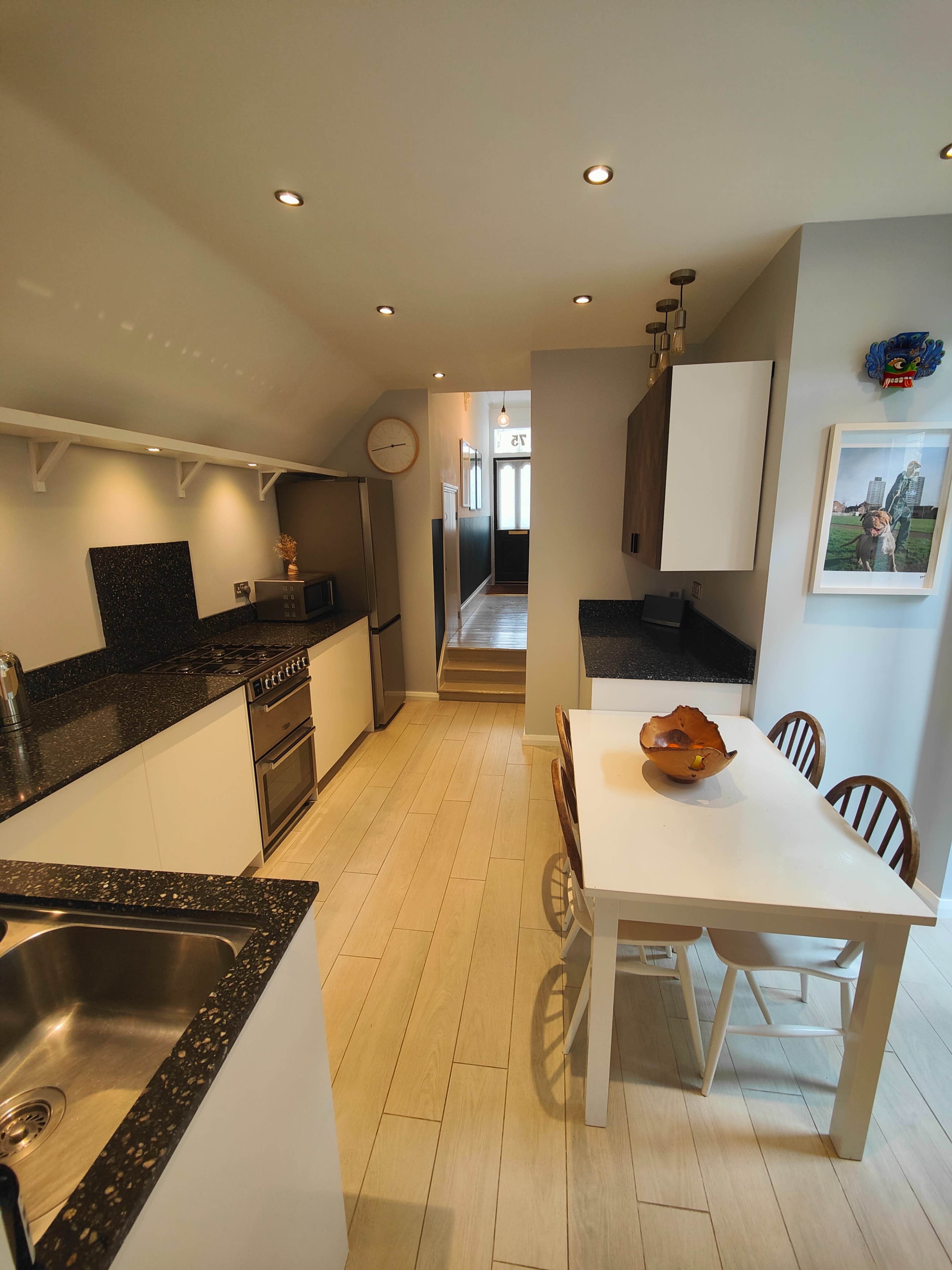 A modern kitchen features black countertops, stainless steel appliances, and a white dining table with chairs.