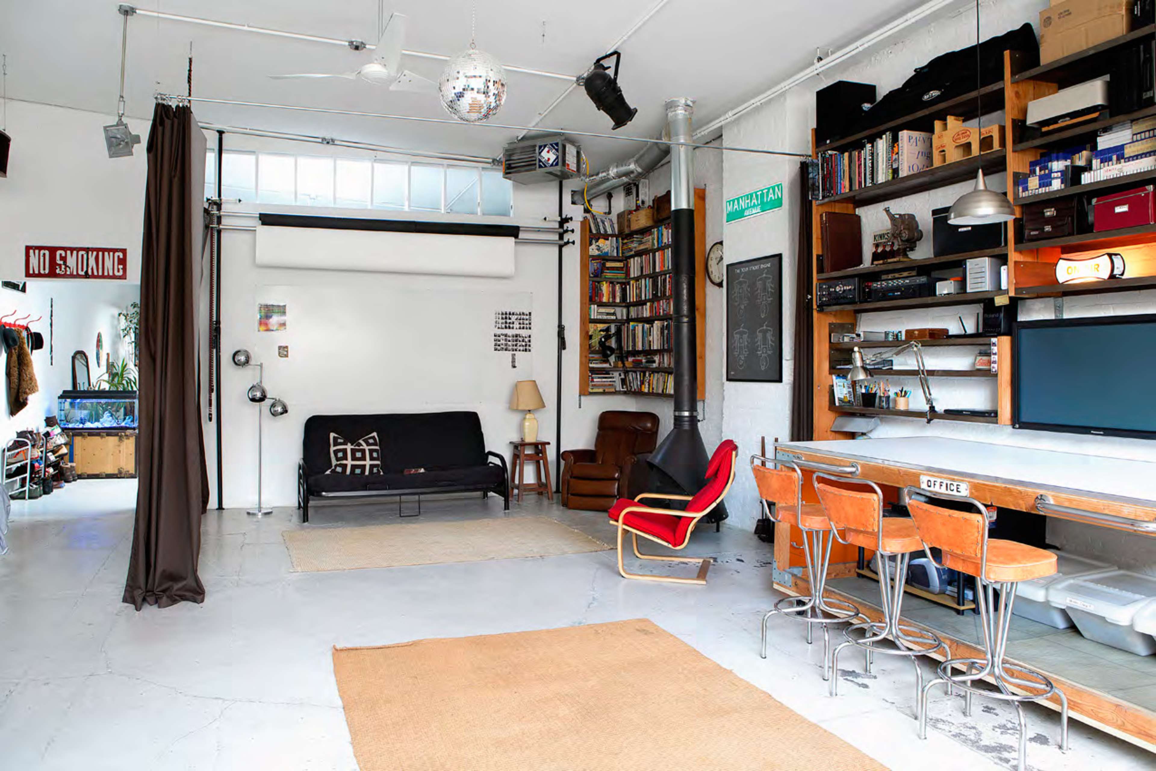 A spacious, modern room with a couch, a chair, a table with chairs, shelves filled with books, and a disco ball hanging from the ceiling.