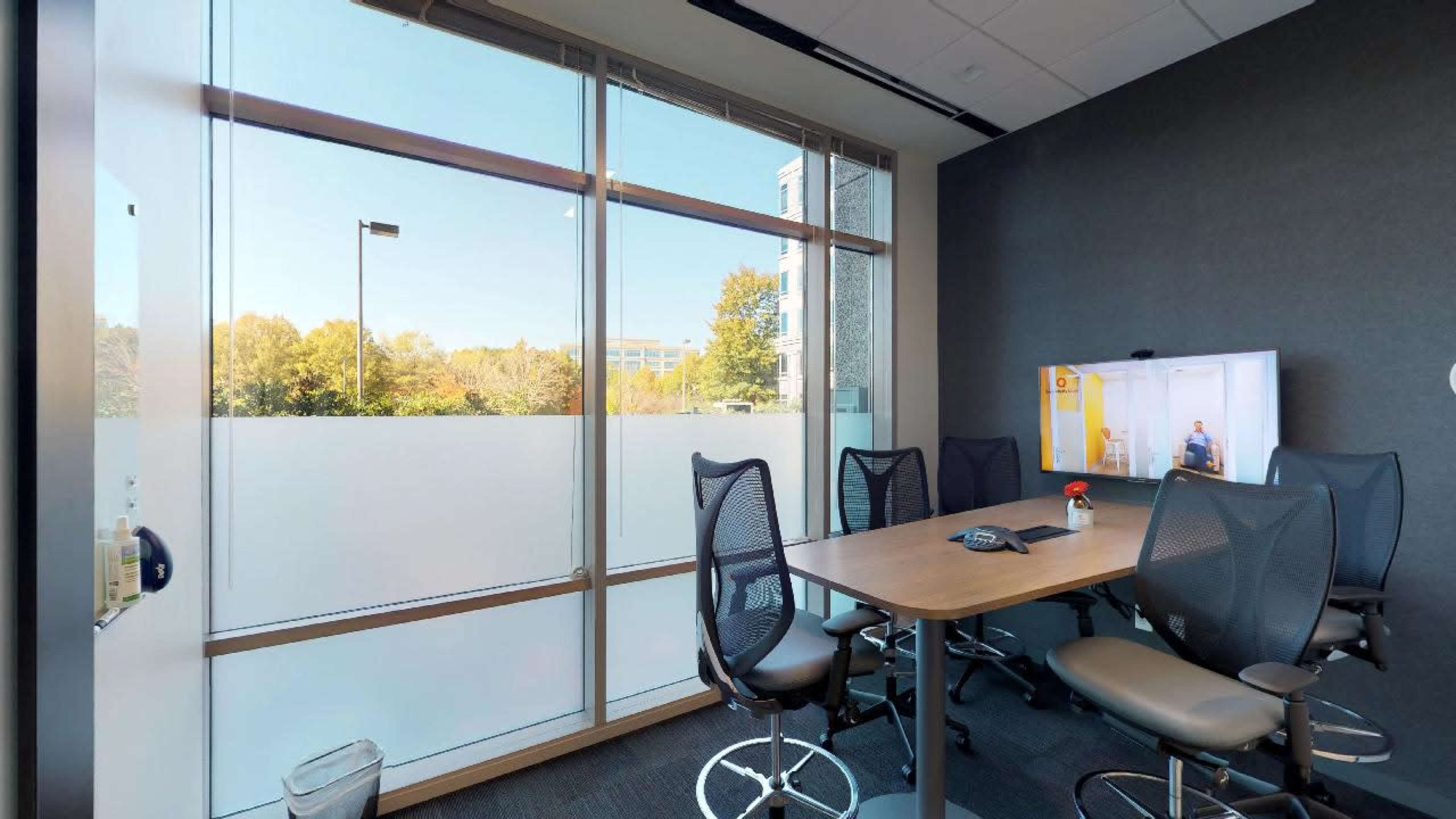 A modern conference room with a large window, a table, and several ergonomic chairs.