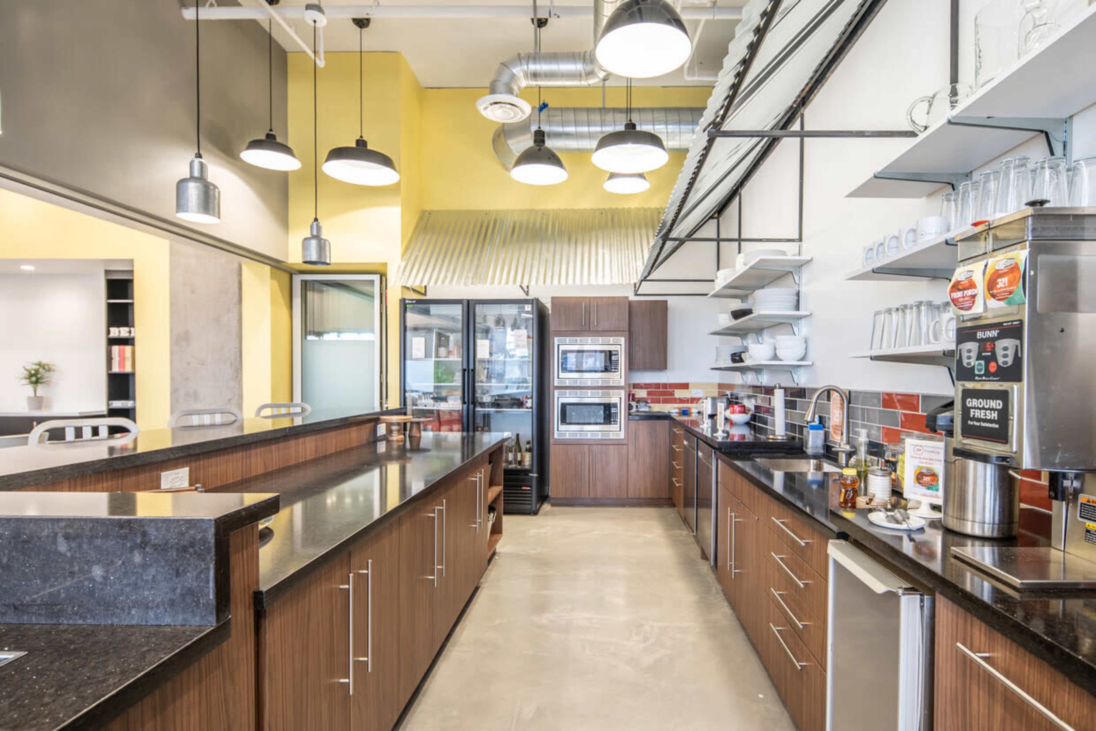 A modern kitchen with dark wood cabinetry, stainless steel appliances, and a spacious layout featuring a long countertop and multiple pendant lights overhead.