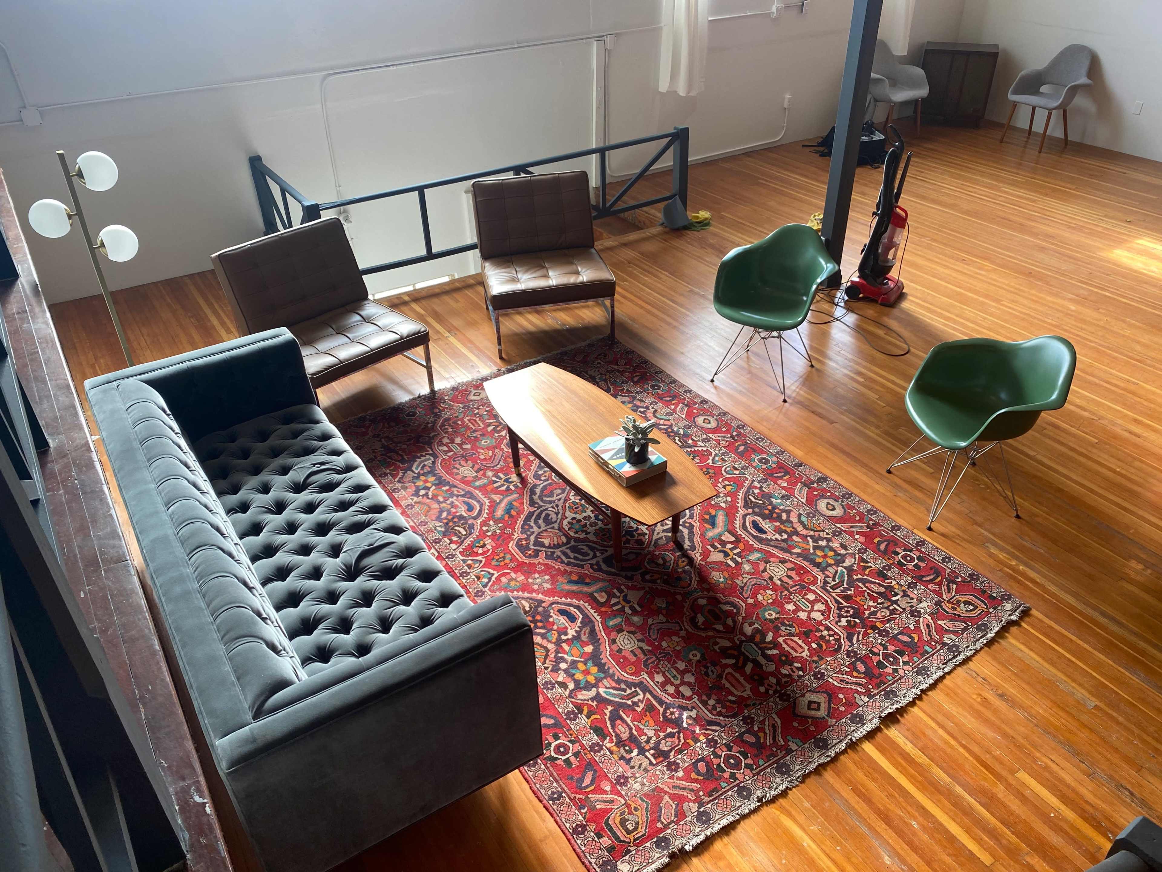 A spacious, wooden-floored room with a seating arrangement that includes a sofa, three chairs, and a coffee table on a patterned rug.