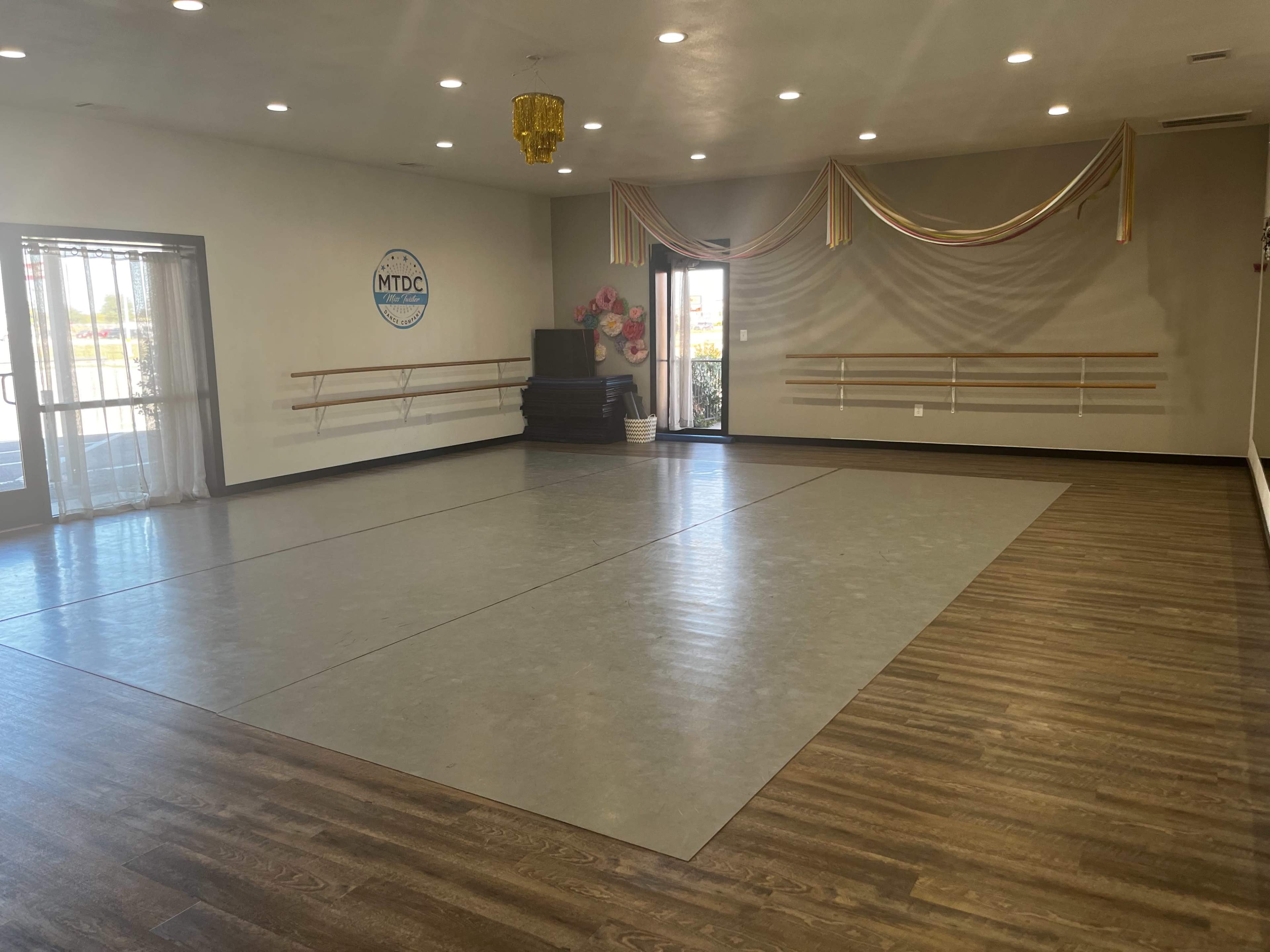 The image shows a spacious dance studio with a mirrored wall, ballet barres, and a decorated entrance.