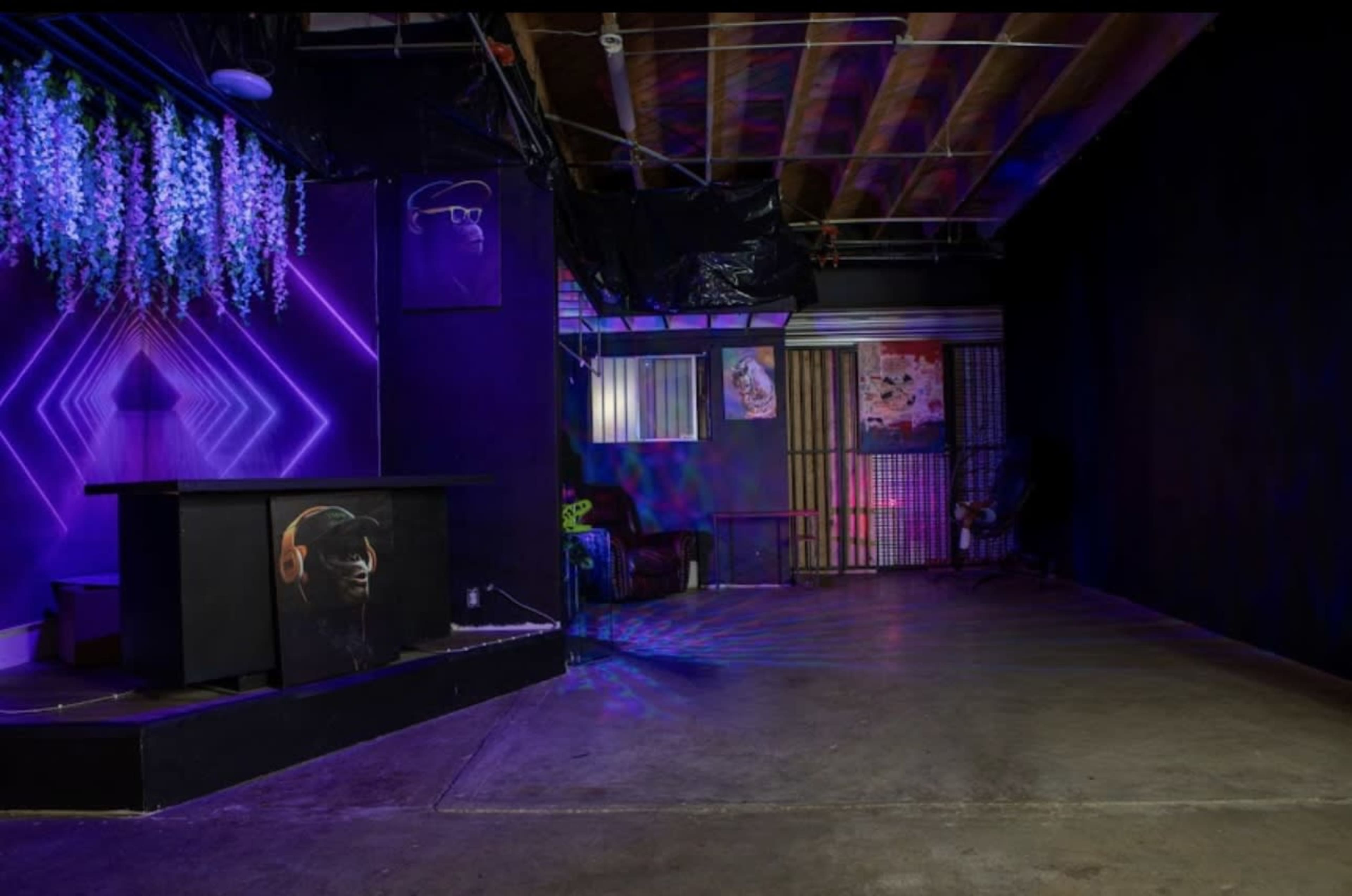 The image shows a dimly lit room with a decorated wall featuring purple lighting, a counter with an artwork, and a seating area in the background.