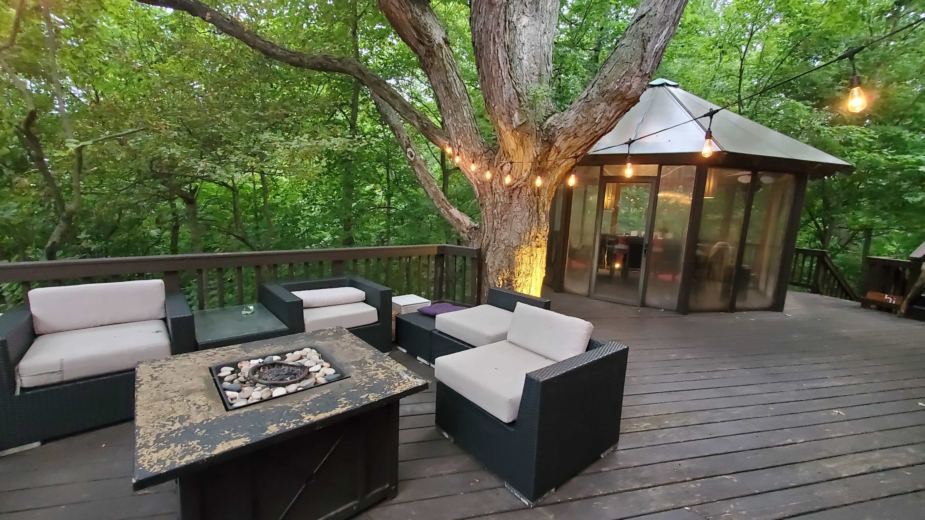 A wooden deck surrounded by trees features modern outdoor furniture and a circular glass-enclosed structure.