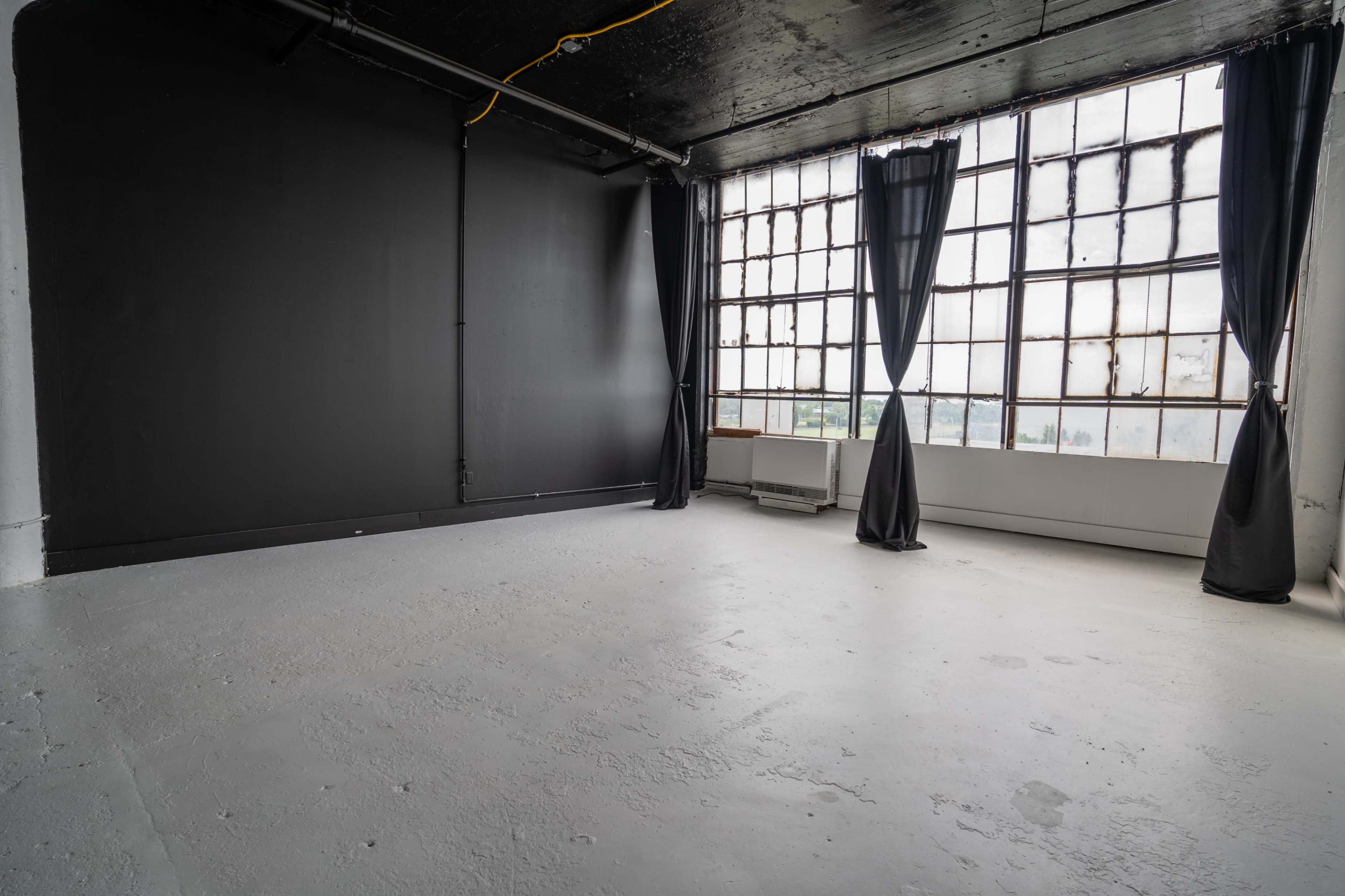 A spacious, empty room with a large window covered by black curtains and a stark black wall.
