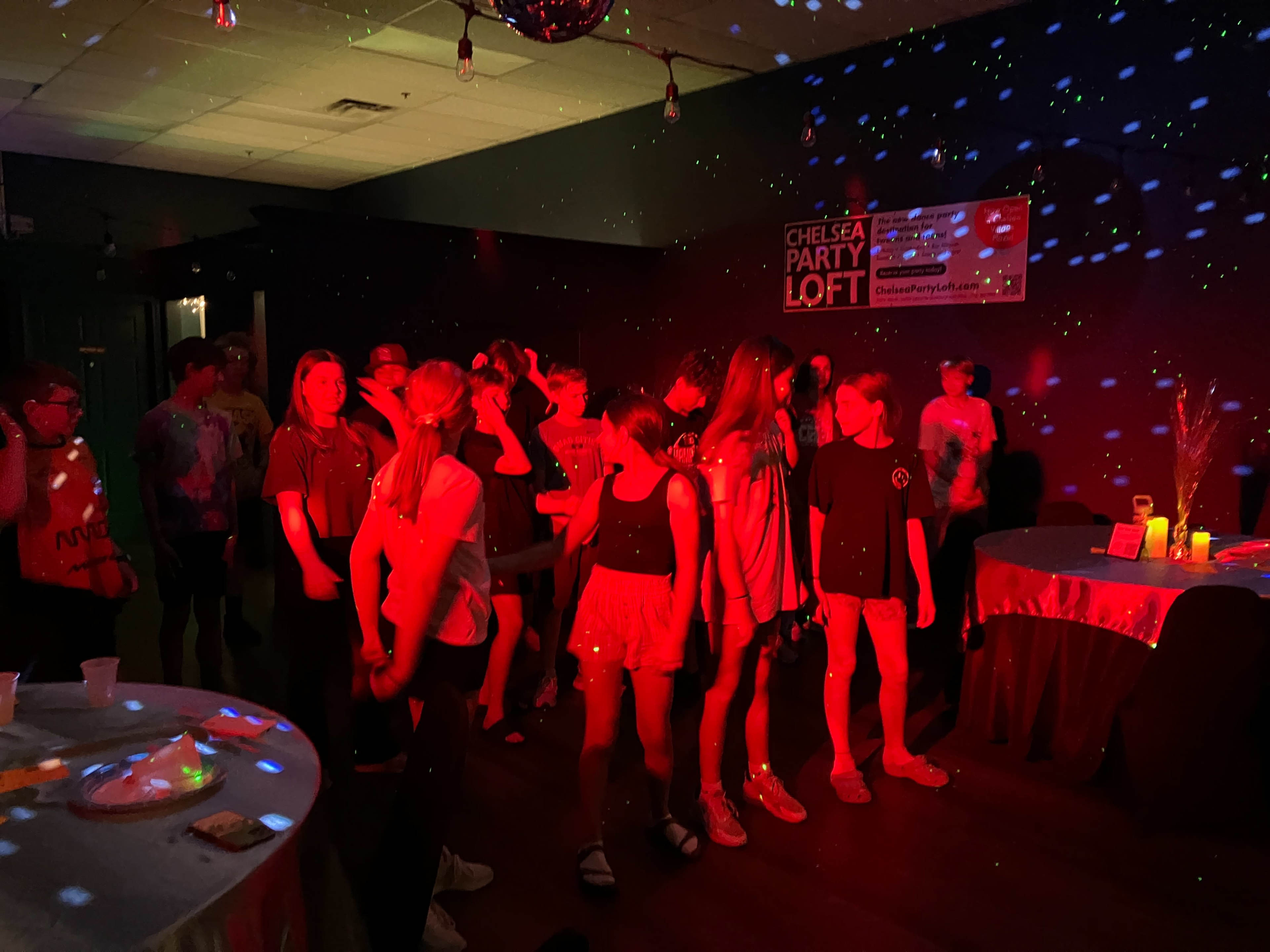 A group of young people are dancing under colorful lights in a party venue.
