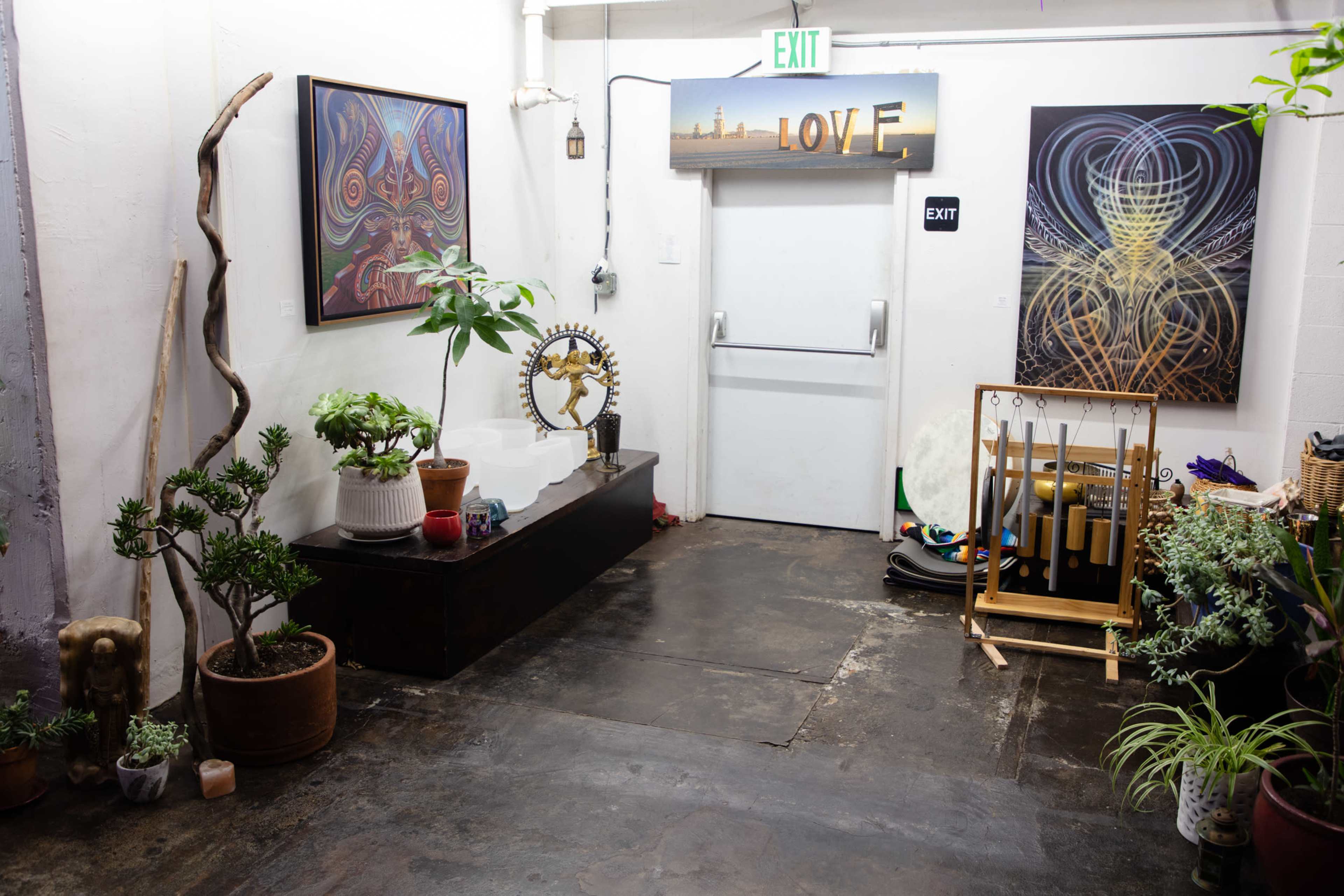 A hallway featuring various plants, artworks on the walls, and a doorway marked "EXIT" alongside an illuminated "LOVE" sign.