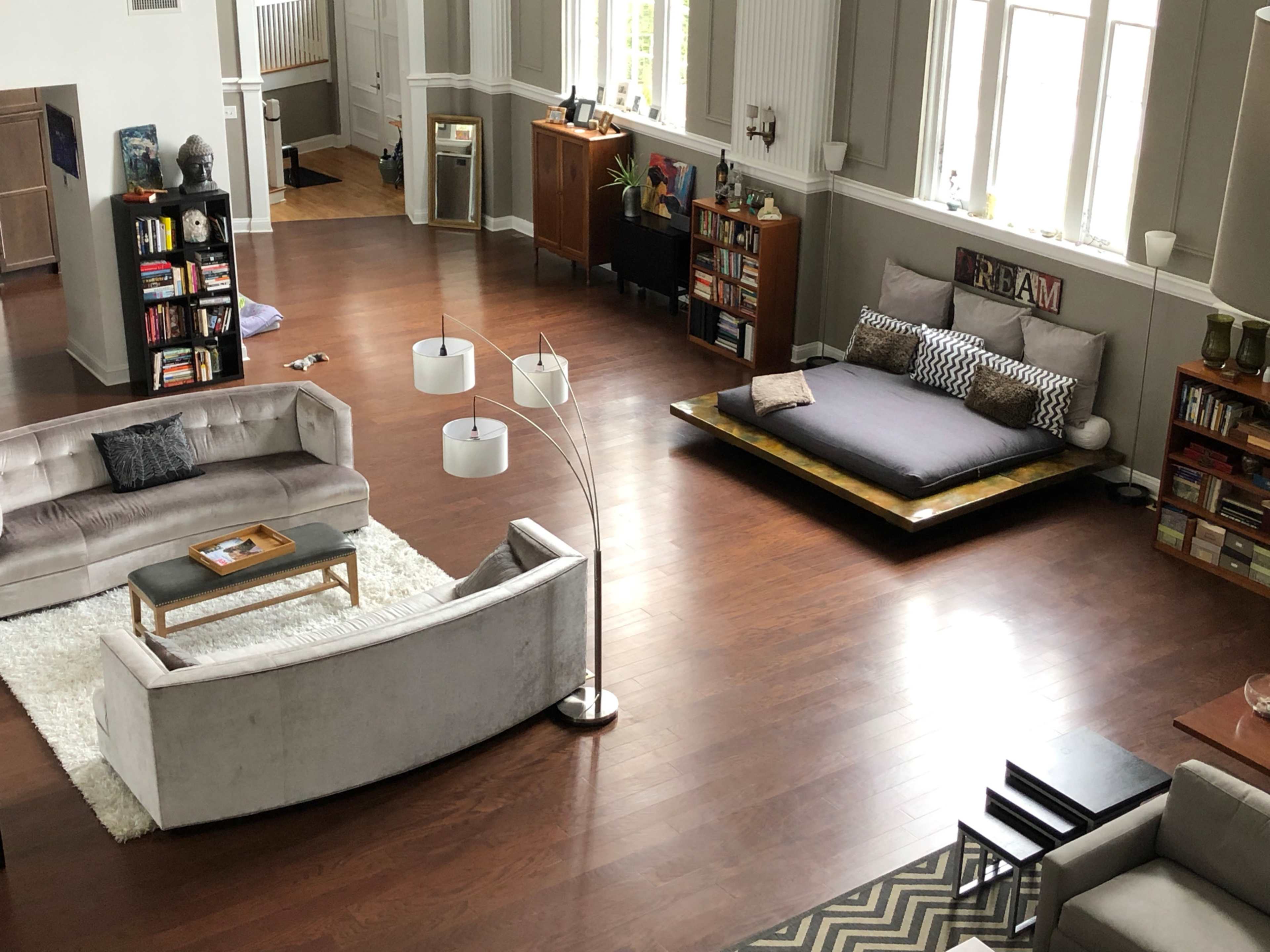 A spacious living area with hardwood floors, two couches, a coffee table, and a large platform bed surrounded by bookshelves and decorative items.