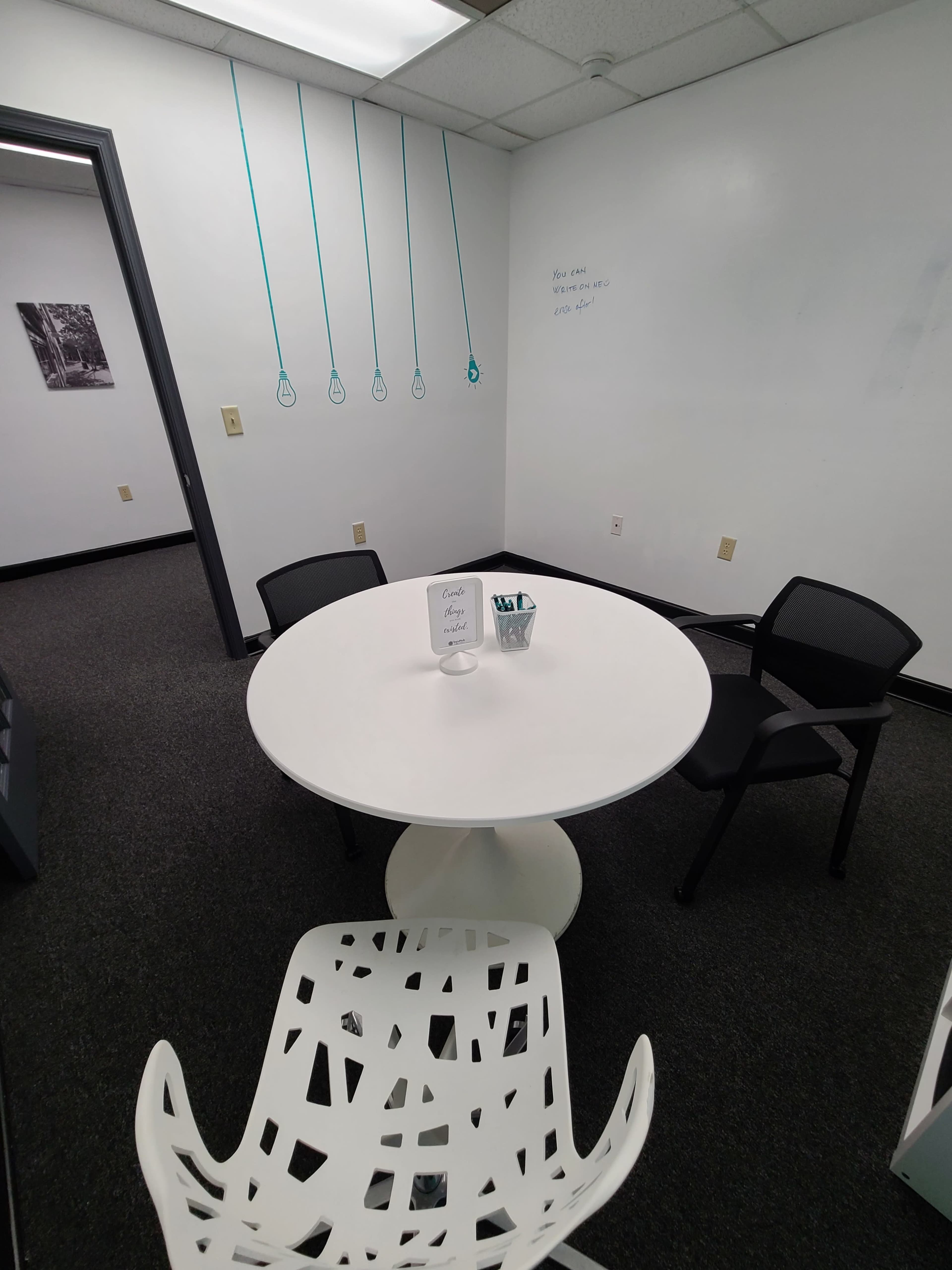 A small office space with a round white table, four black chairs, and dangling decorative elements on the wall.
