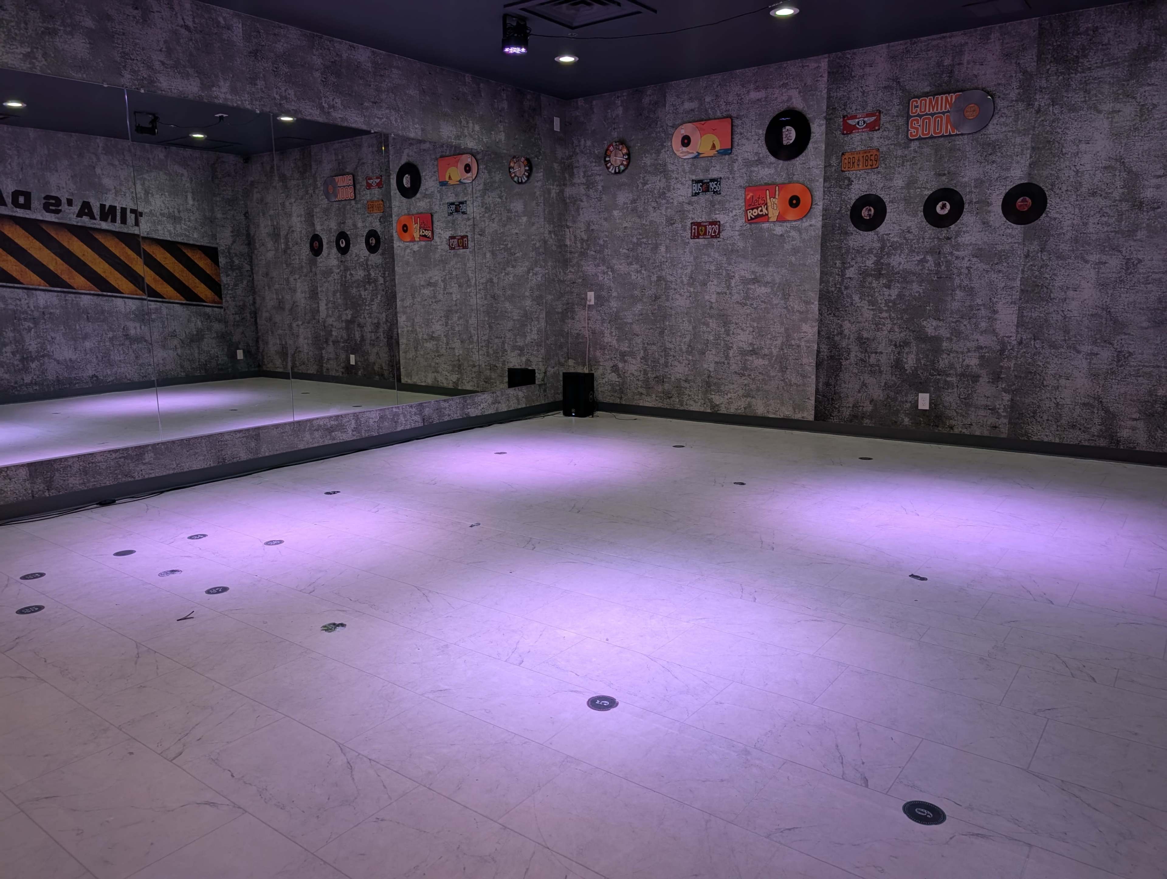 The image shows an empty dance studio with gray walls, a large mirror, and colorful vinyl record decorations.