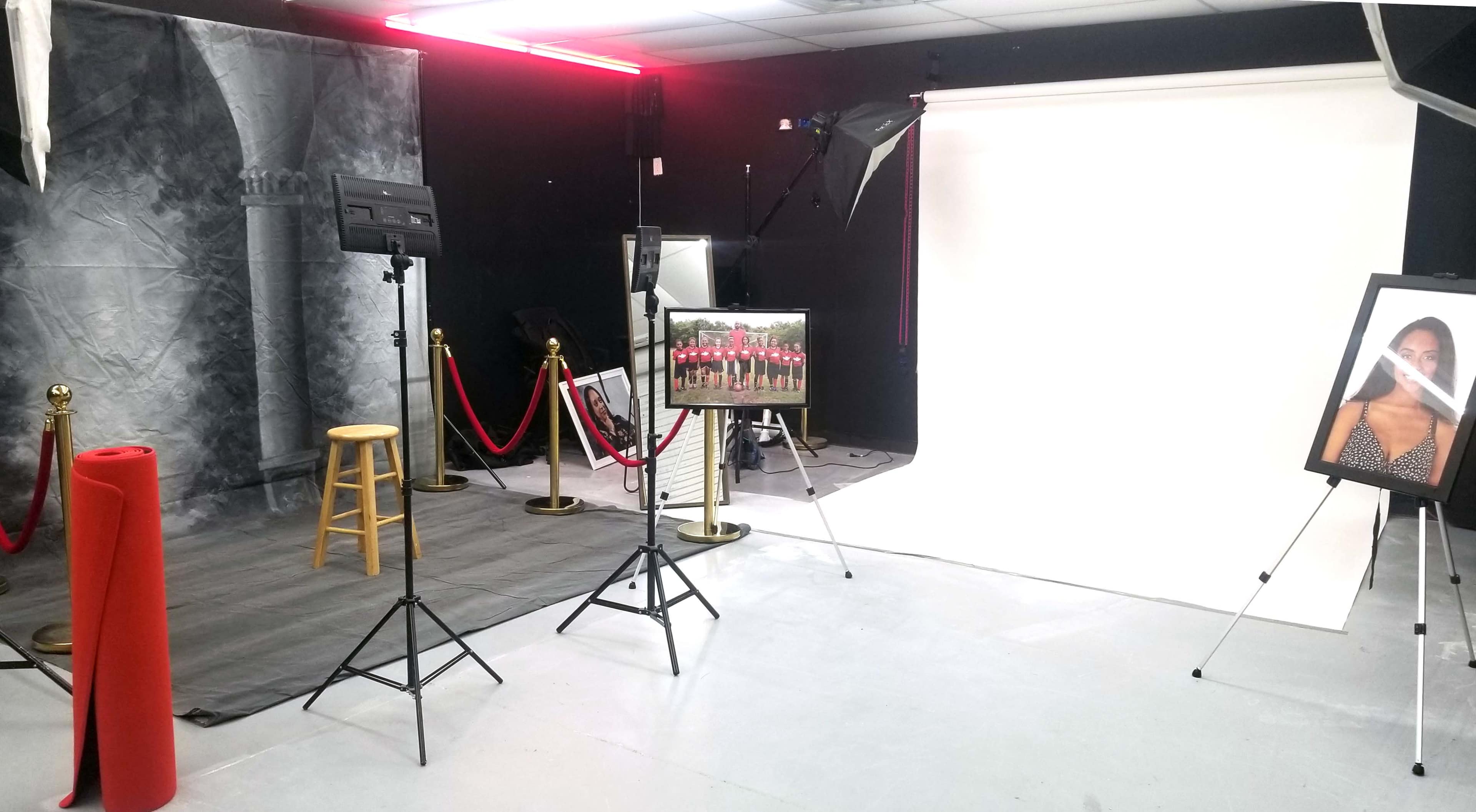 A photography studio setup with a backdrop, a stool, lighting equipment, and a framed photograph on display.
