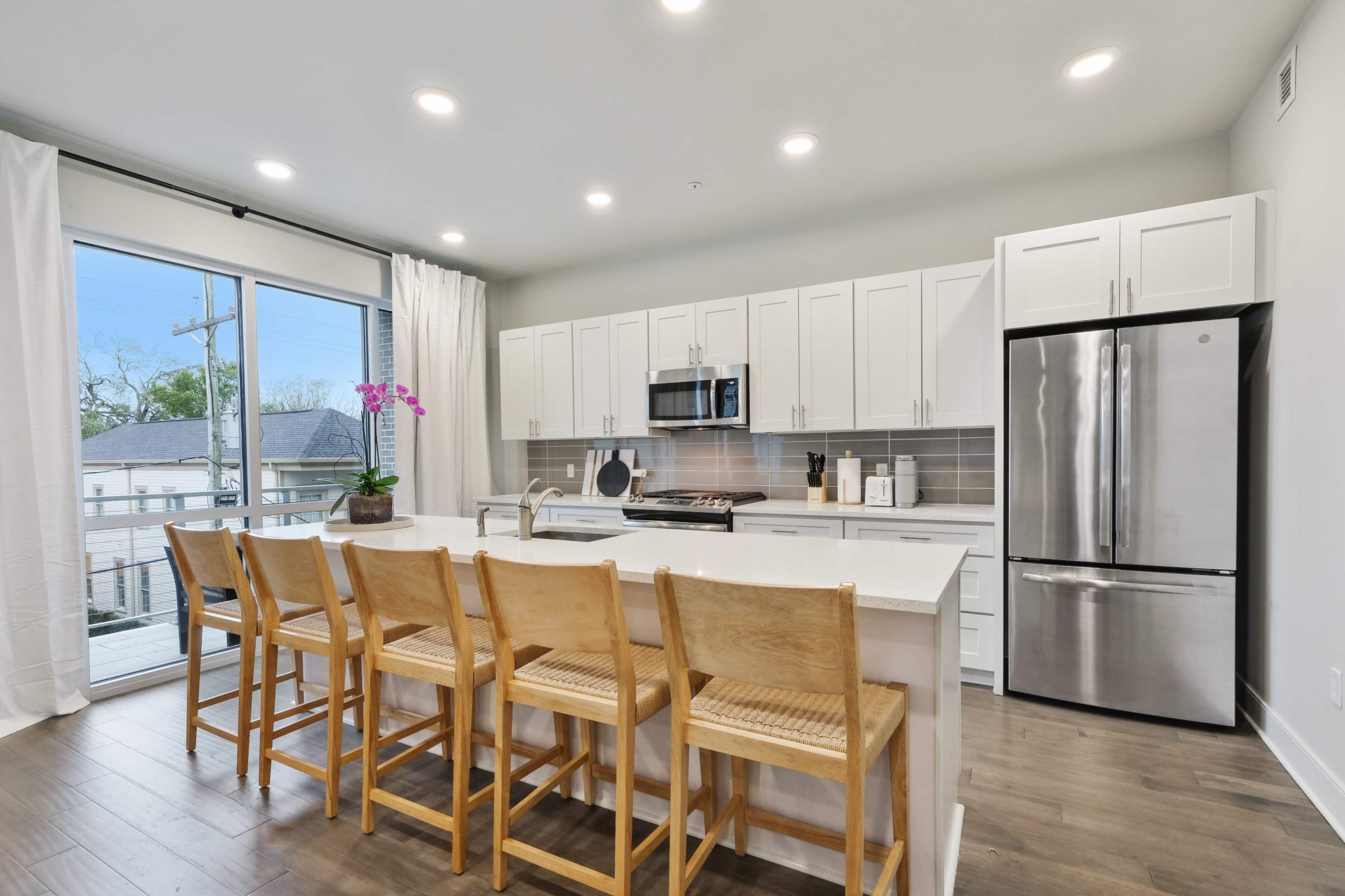 A modern kitchen features white cabinetry, stainless steel appliances, and a large island with seating for six.