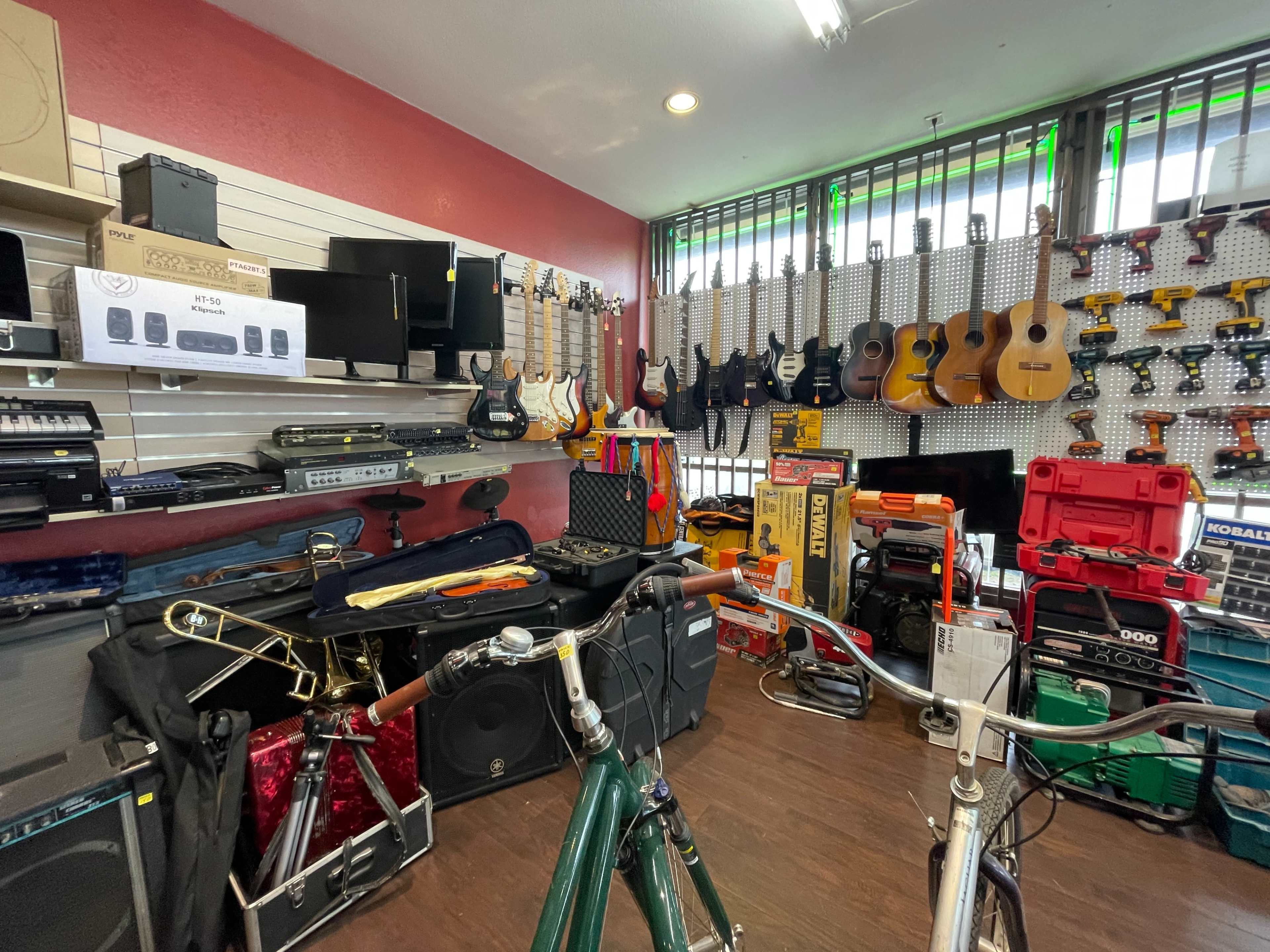 The image shows a music store displaying a variety of musical instruments and equipment, including guitars, amplifiers, and percussion instruments, alongside tools and bicycle frames.