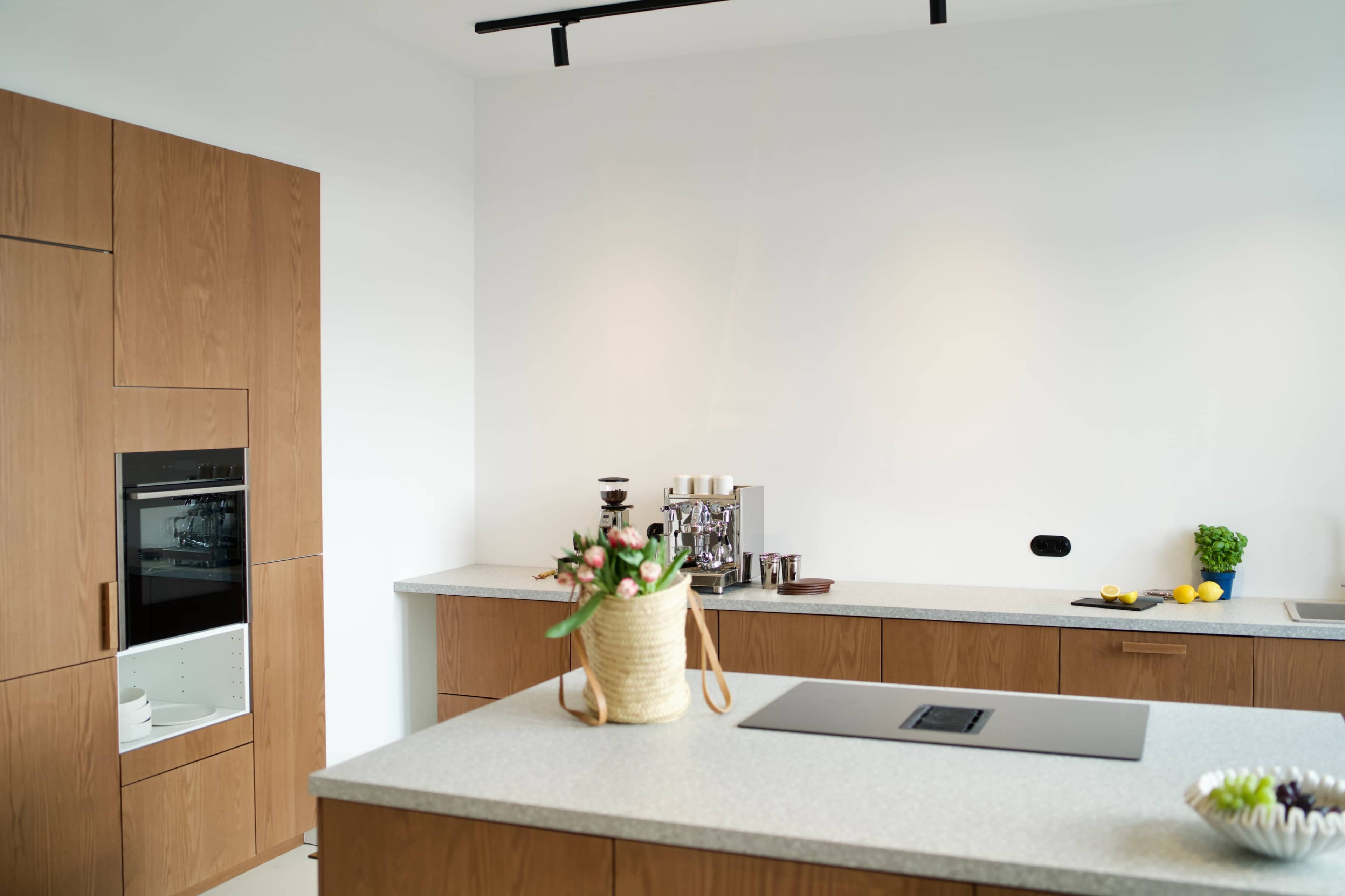 The image shows a modern kitchen with wooden cabinetry, a countertop, and a range of kitchen appliances and fresh ingredients.