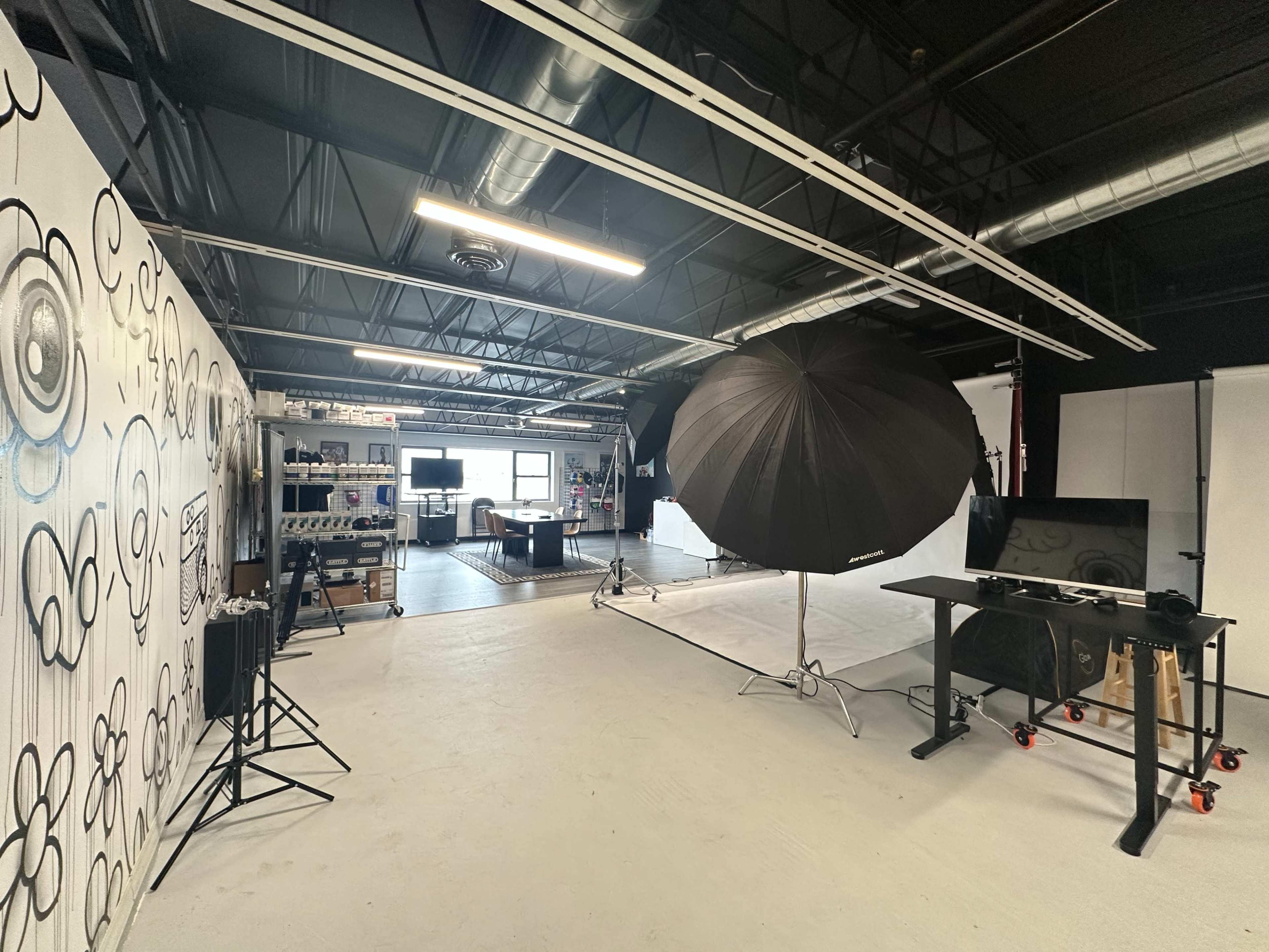 A photography studio featuring a large umbrella light, backdrop, and various equipment arranged in a spacious room with industrial lighting.
