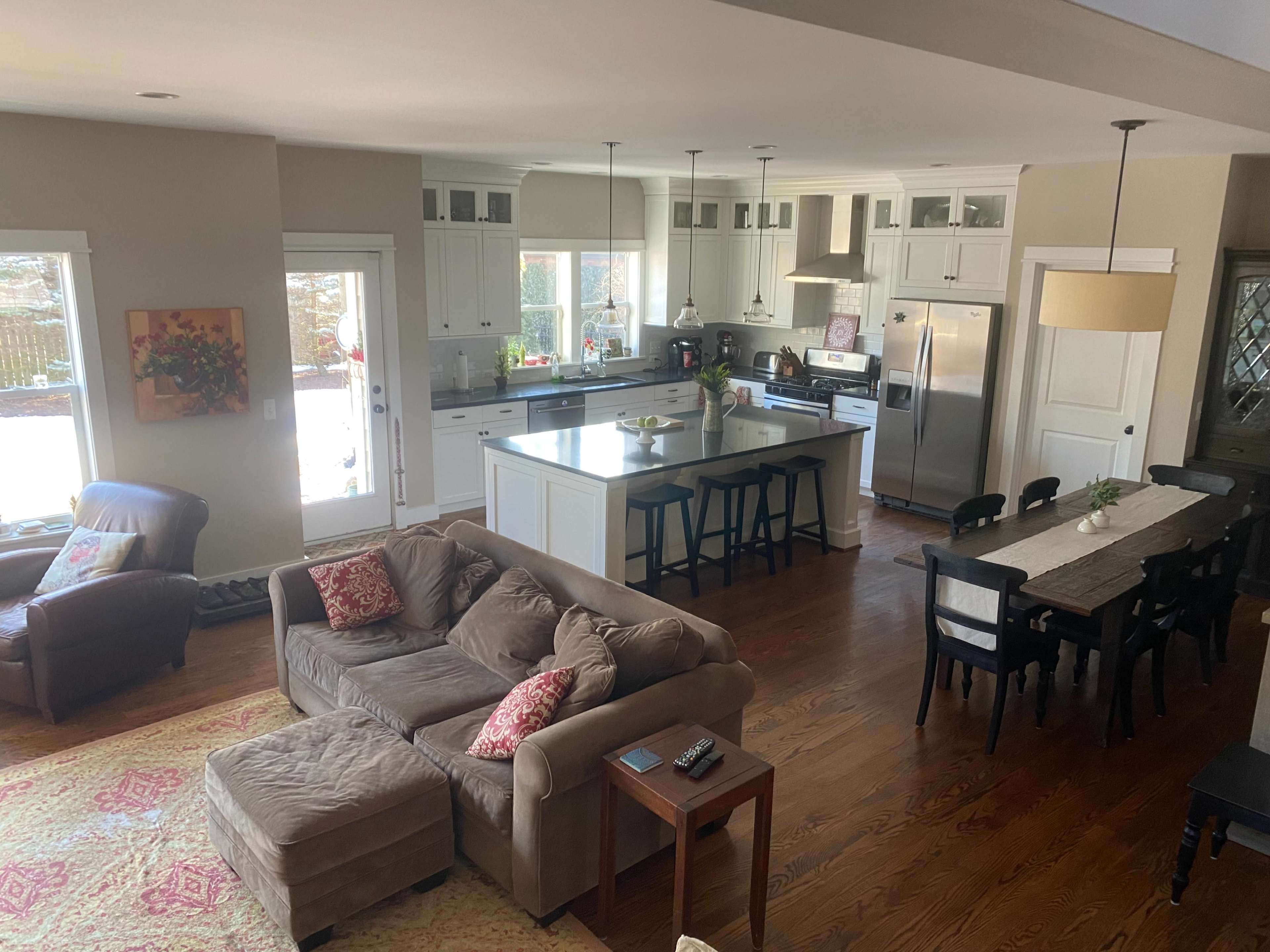 A spacious kitchen and dining area features white cabinetry, wooden flooring, and a mix of seating options, including a sectional sofa and a dining table.