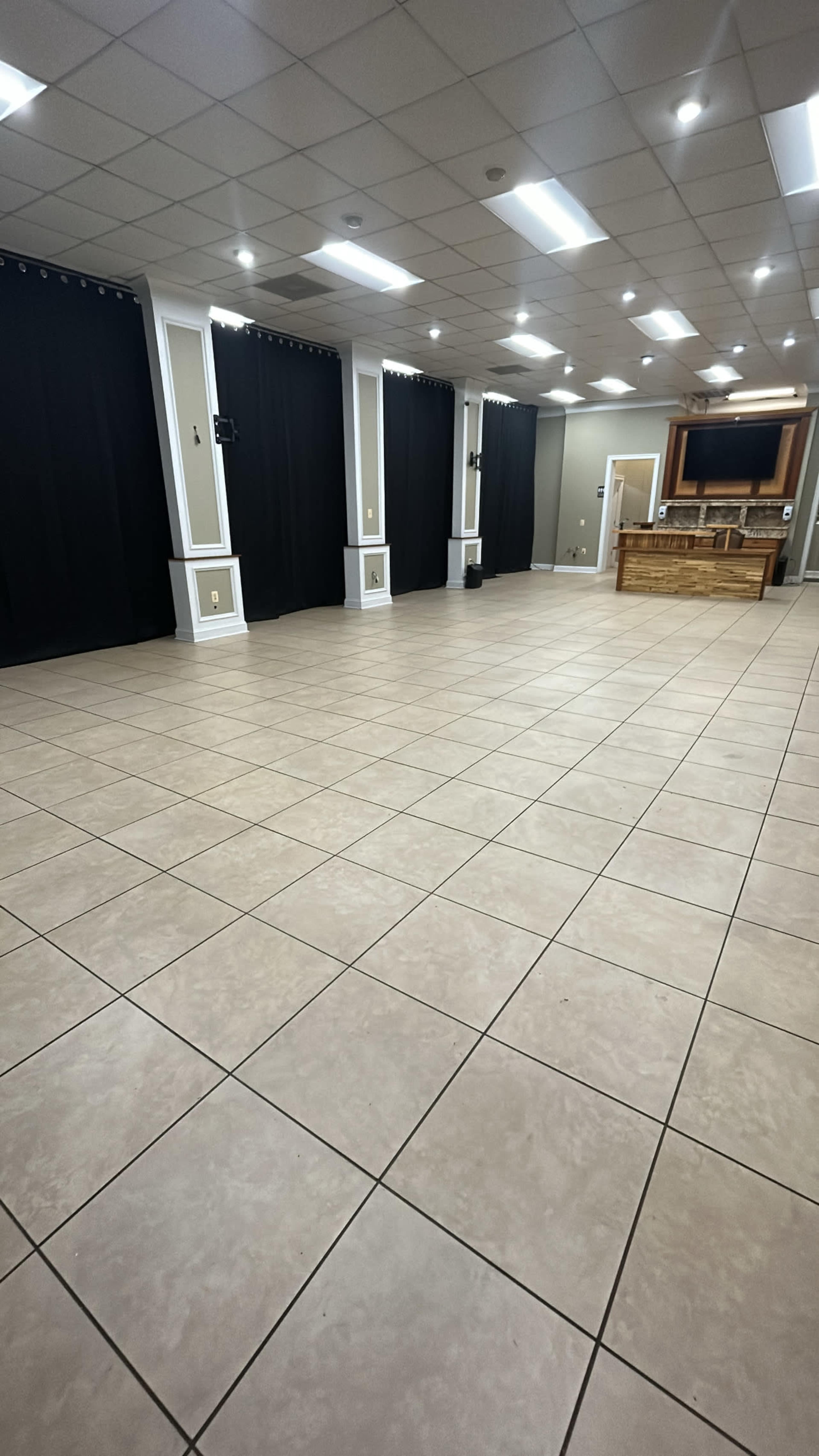 A spacious room with tiled flooring, black curtains on the walls, and a wooden structure at the far end.