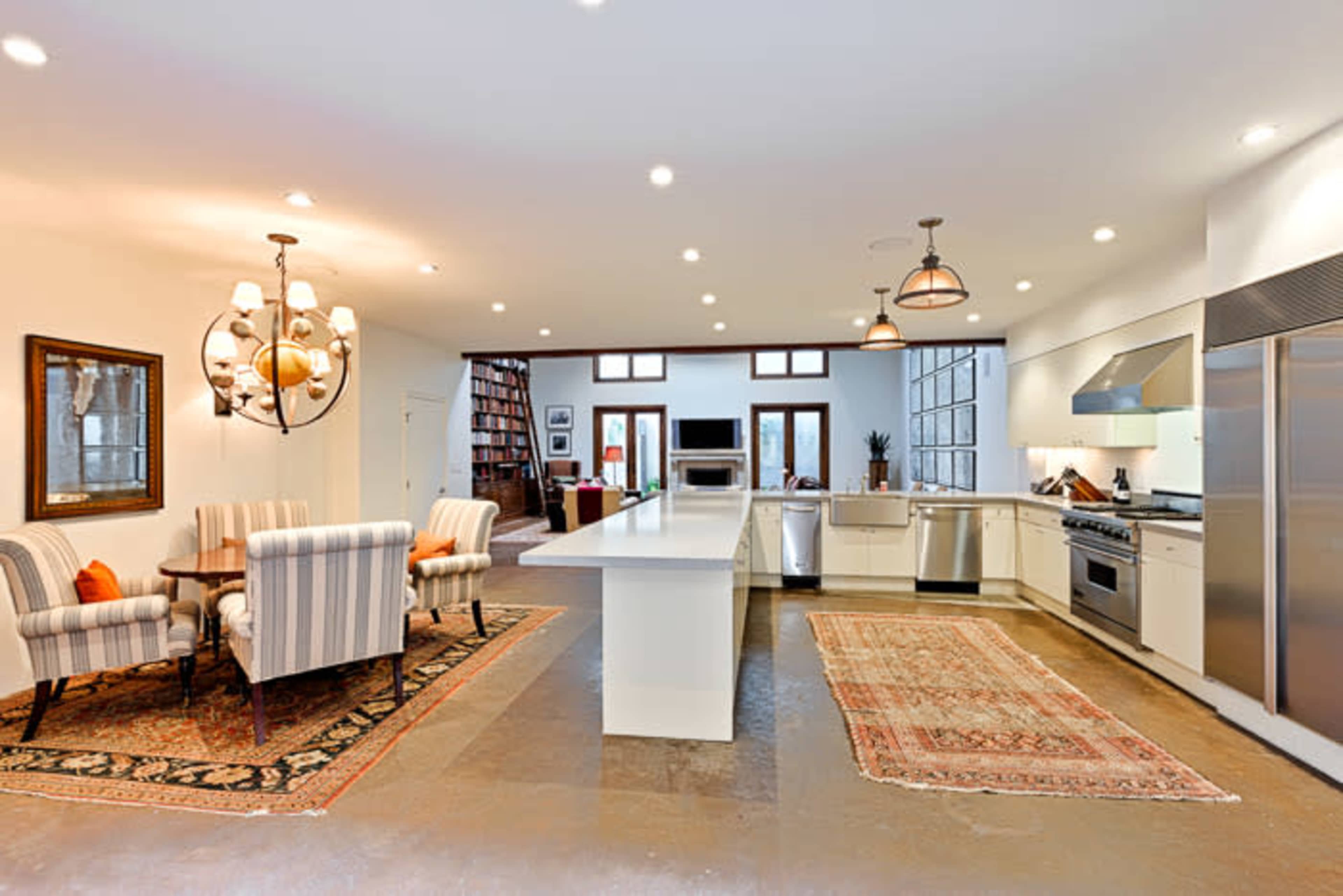 The image shows a modern kitchen with an island, stainless steel appliances, and a dining area featuring striped chairs next to a patterned rug.