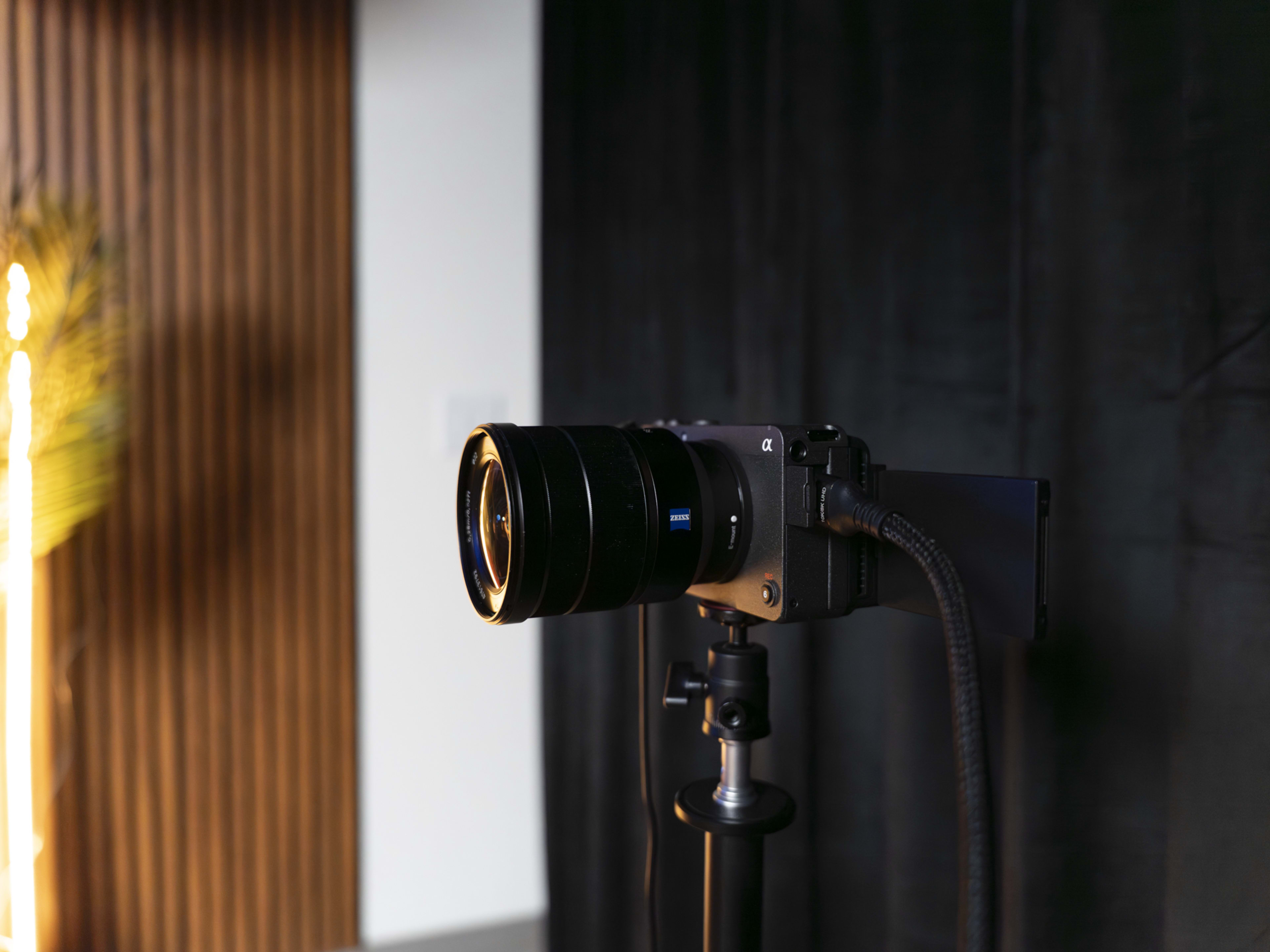 A camera with a large lens is mounted on a tripod in front of a dark backdrop.