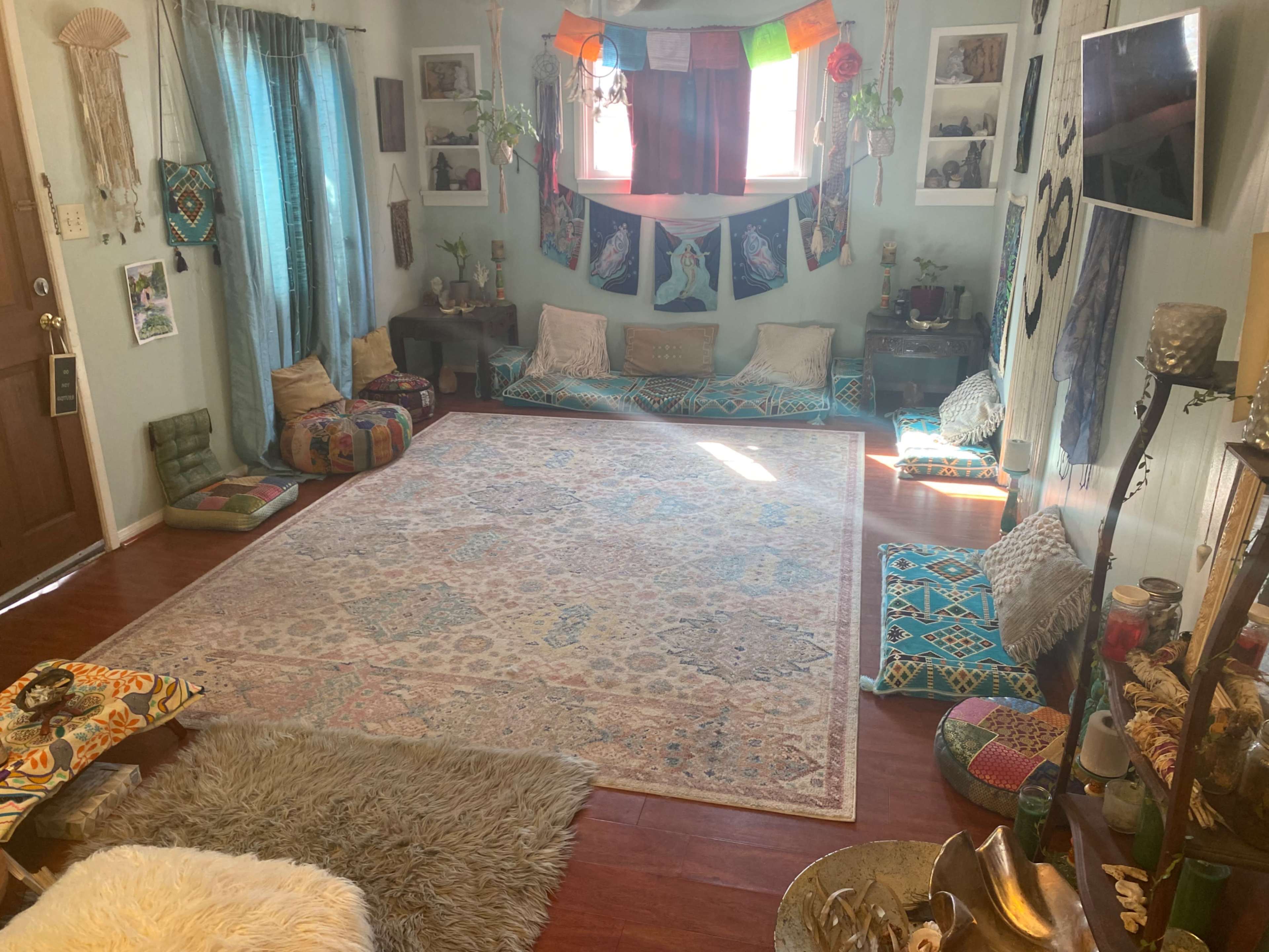 A cozy, decorated room with colorful cushions, a large area rug, and various wall hangings.