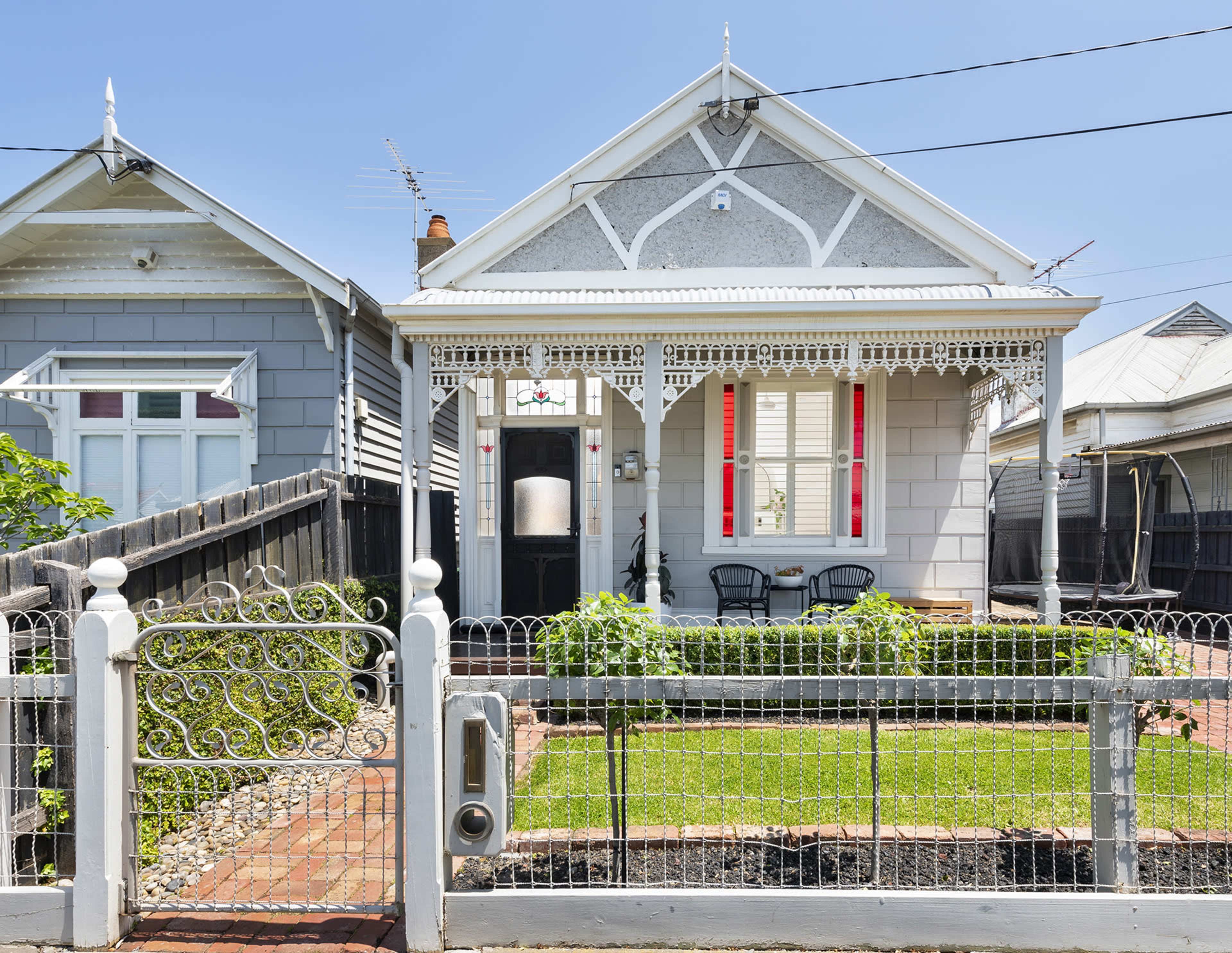 A vintage-style house with a decorative fence, a well-kept front garden, and a porch with two chairs.