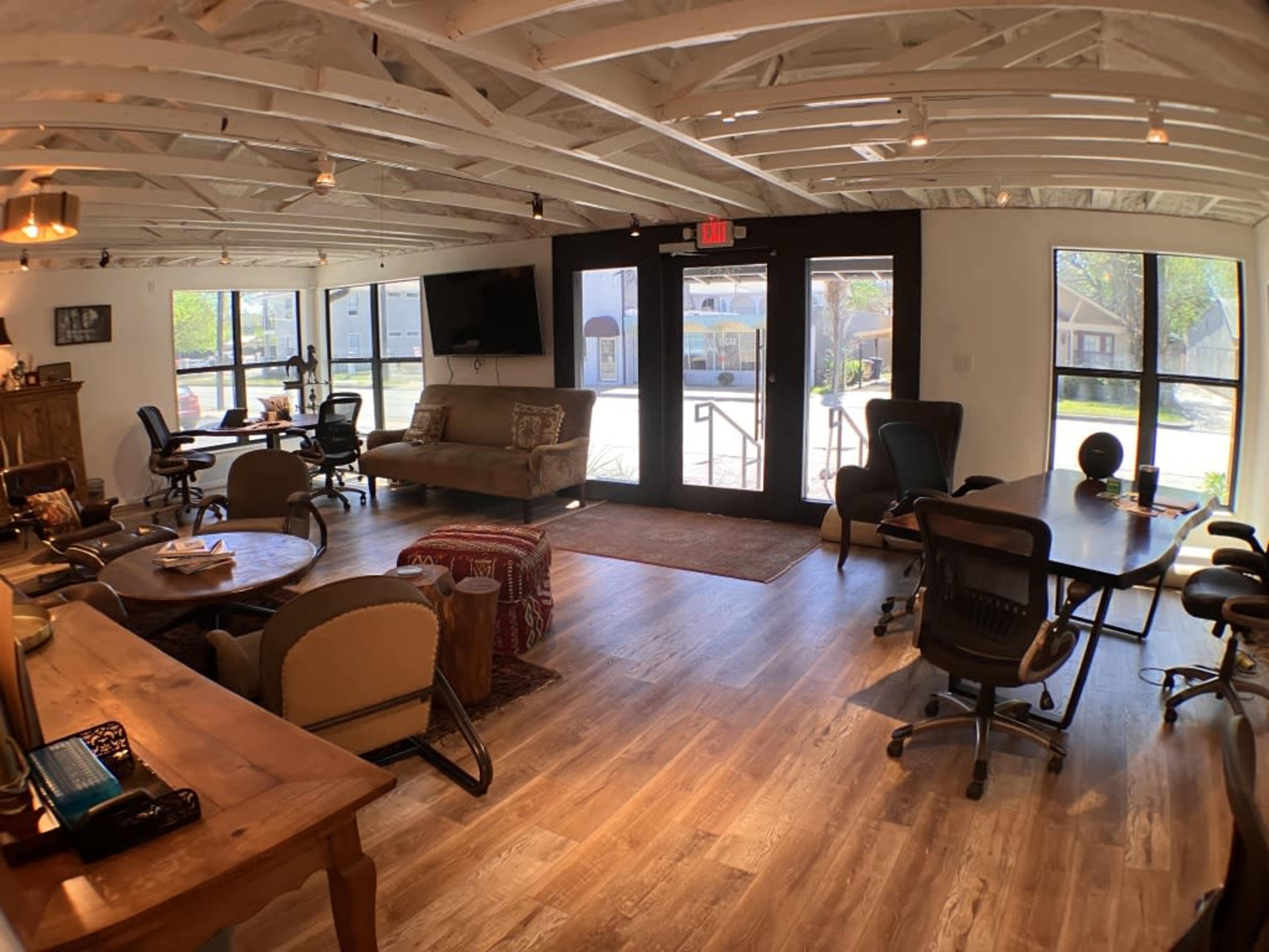 A spacious office with wooden floors, a mix of seating areas, and large windows allowing natural light to enter.