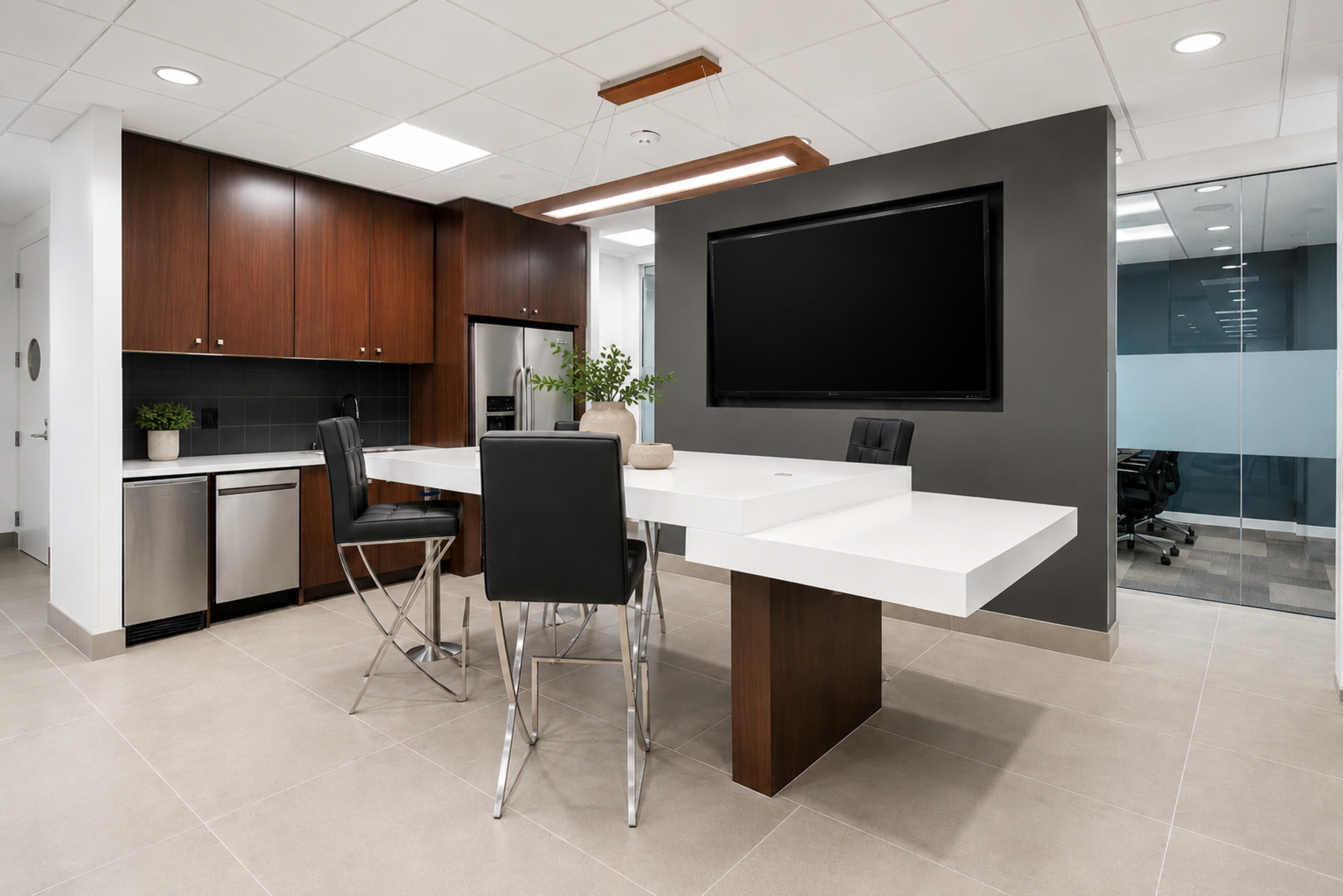 The image shows a modern kitchen area with a white table and black chairs, wooden cabinets, and a wall-mounted television.