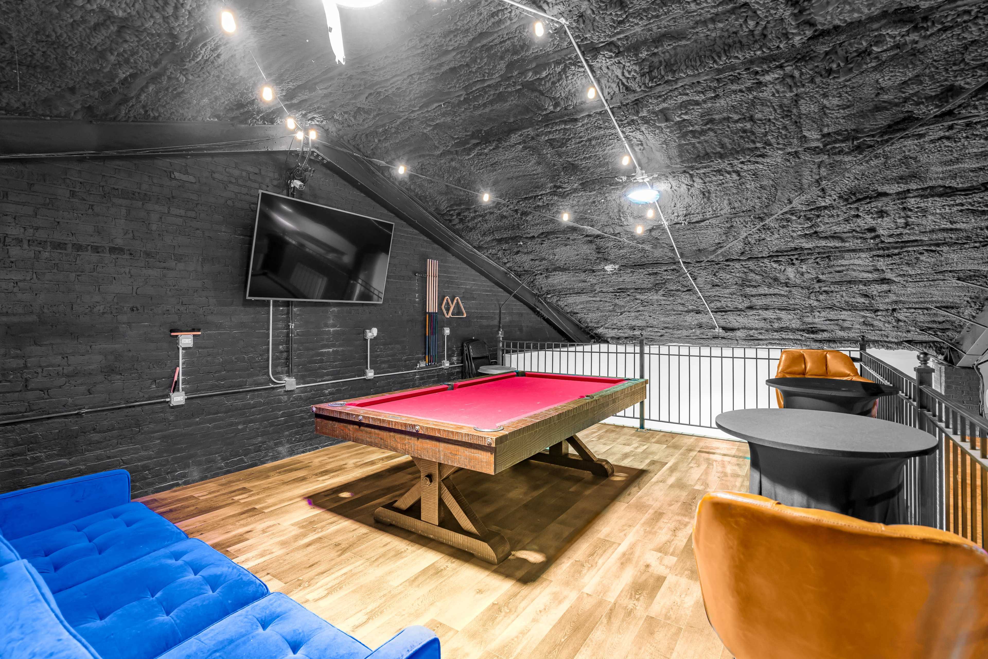 A game room features a billiard table, a large television, and seating areas with modern furniture under a sloped ceiling.