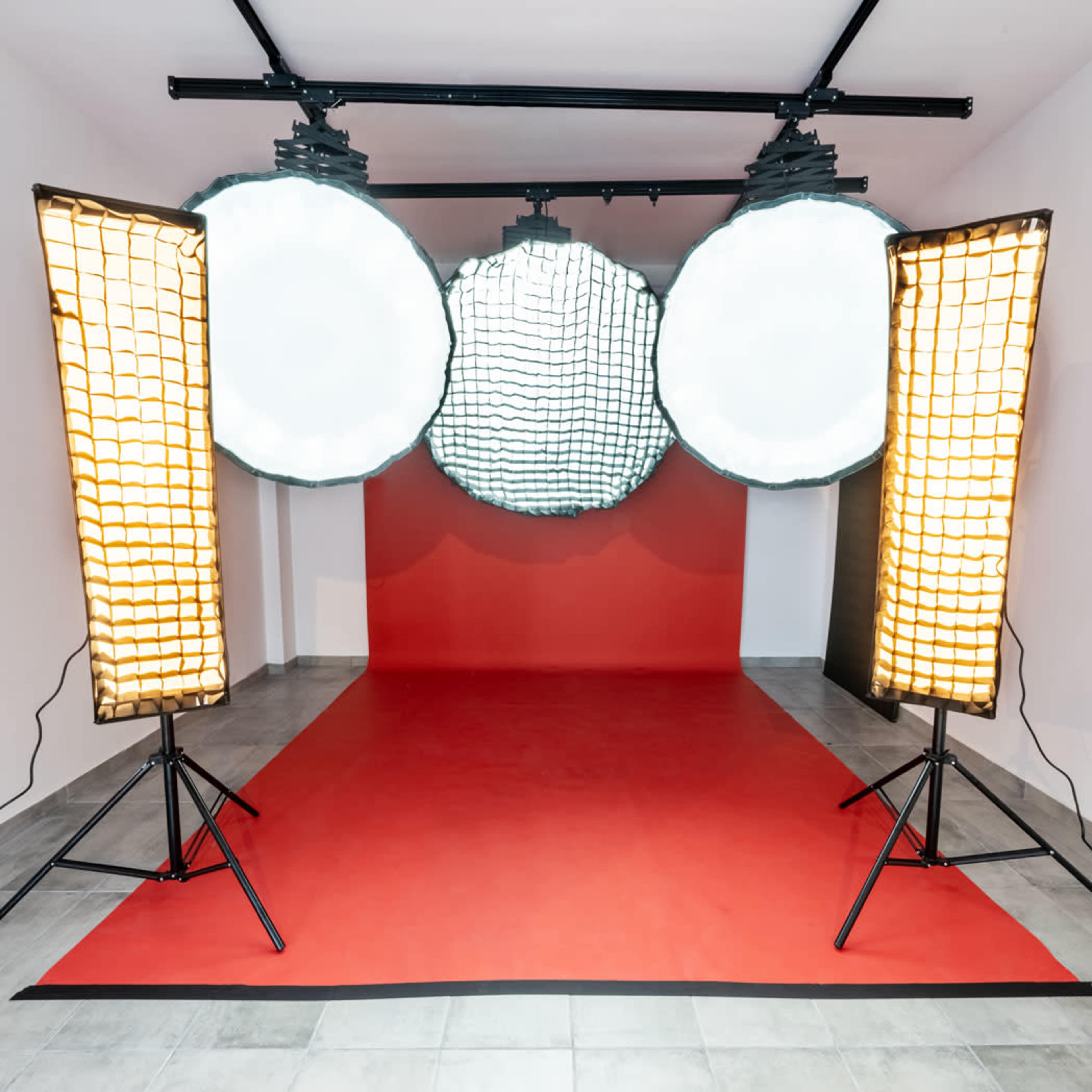 The image shows a photography studio with a red backdrop and three large softbox lights on a stand.