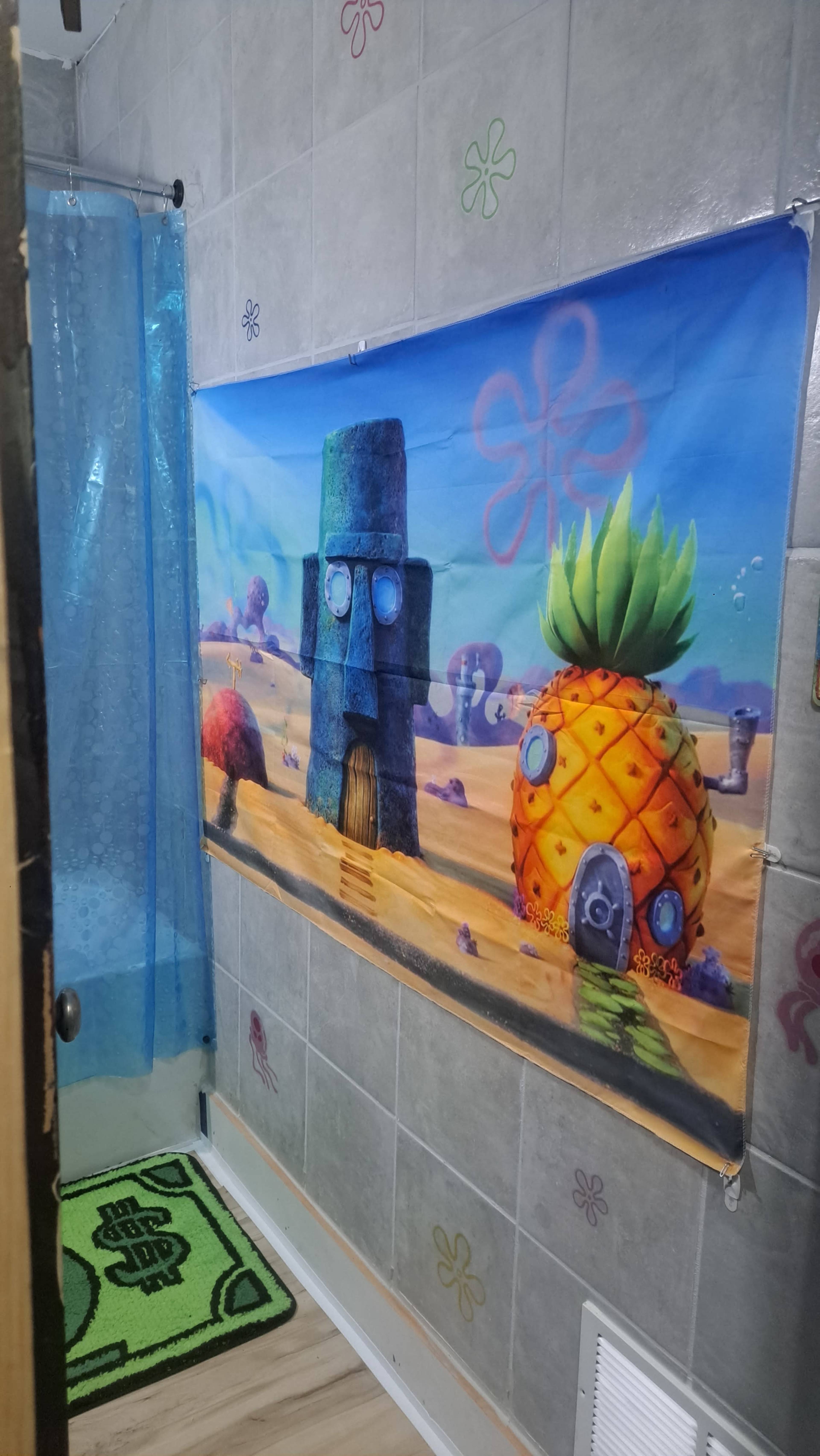 The image shows a bathroom with a colorful wall banner depicting SpongeBob SquarePants' pineapple house and Squidward's house.