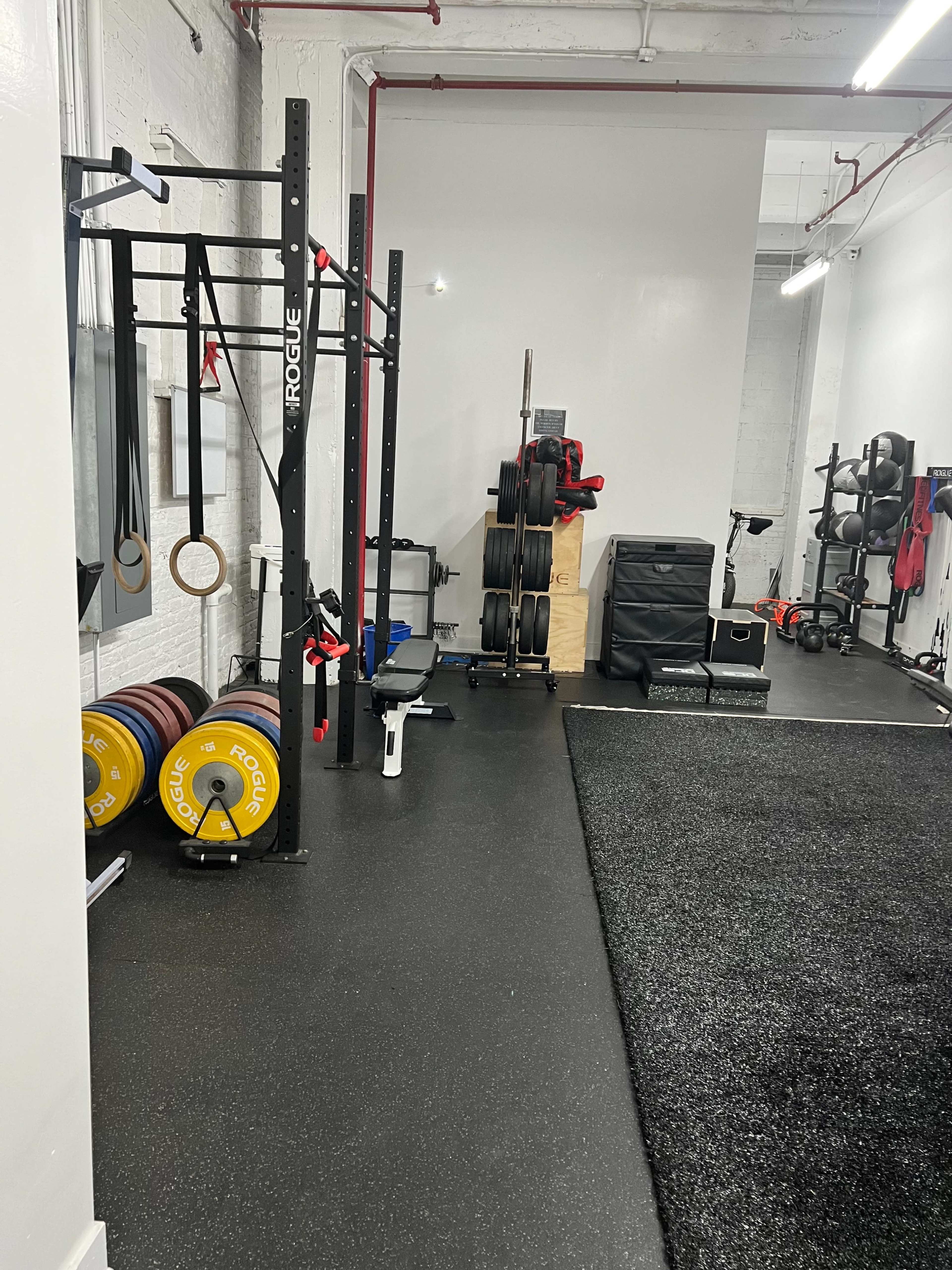 A gym interior featuring a weightlifting rack, barbells, and various fitness equipment organized against the wall.