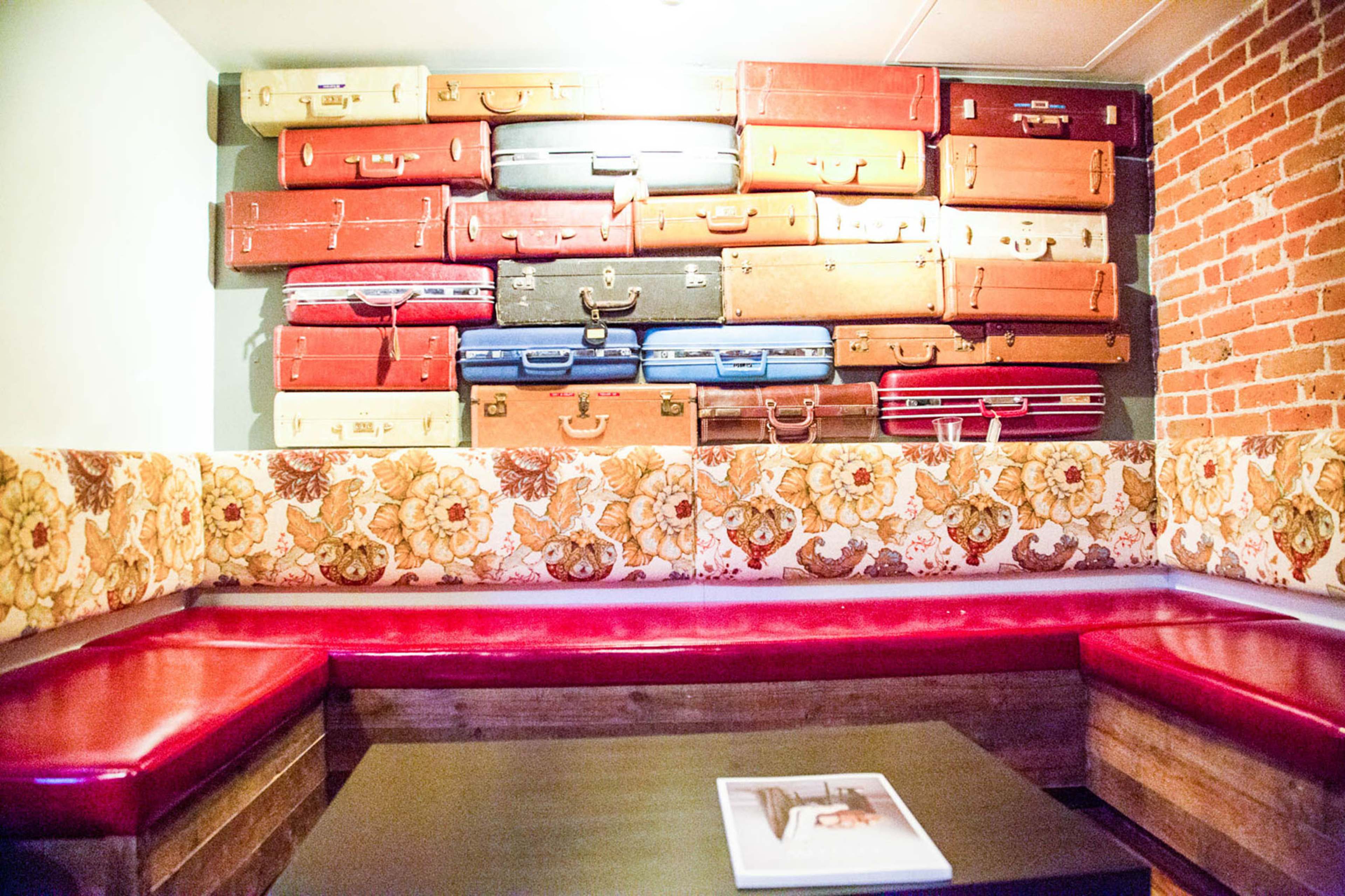 A cozy seating area with a red cushioned bench against a wall decorated with an arrangement of vintage suitcases.