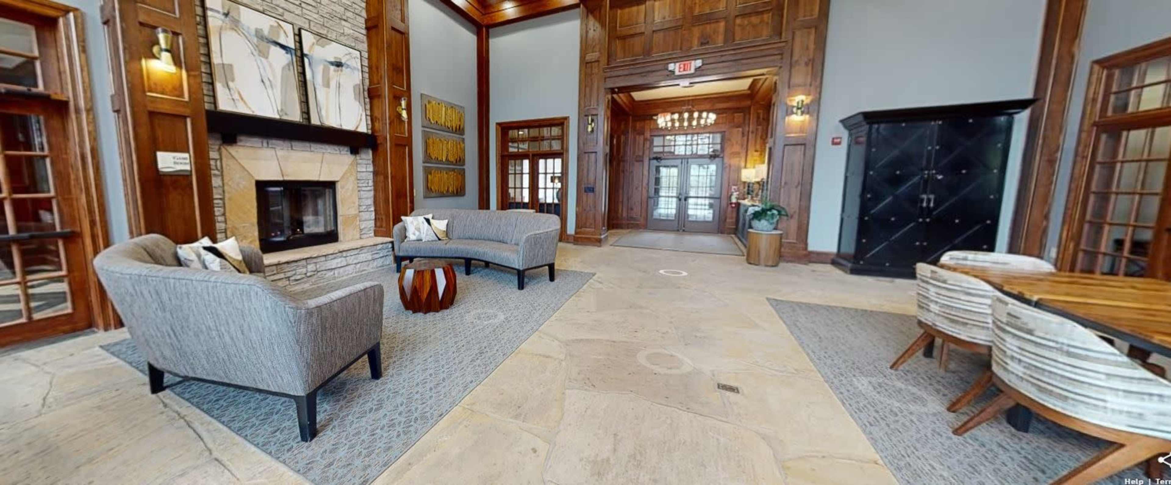 A lobby area with two gray sofas, a wooden coffee table, a fireplace, and a dining table, all set against a backdrop of wooden walls and large windows.
