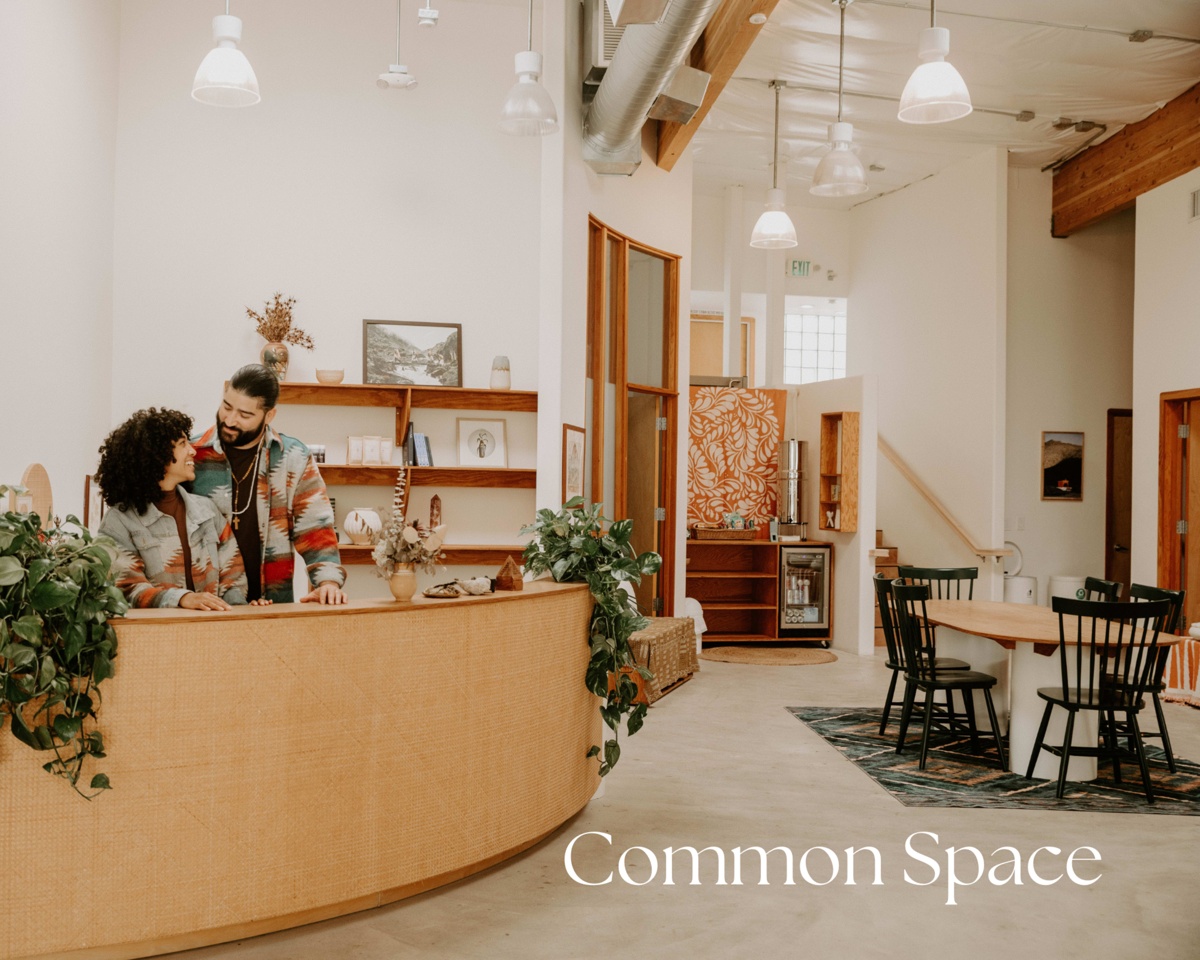 A couple stands at a reception desk in a bright, open common area featuring wooden accents and various seating options.