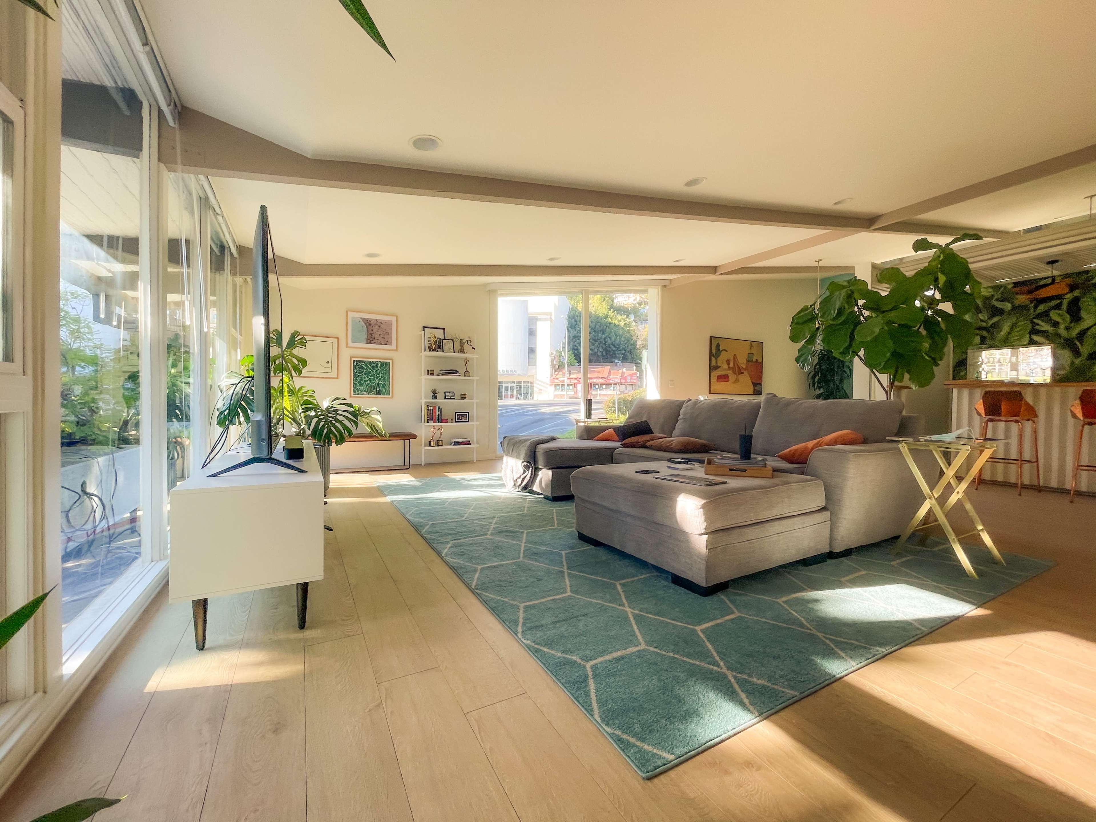 A well-lit, modern living room featuring a gray sectional sofa, a geometric area rug, and large windows that overlook a landscaped outdoor space.