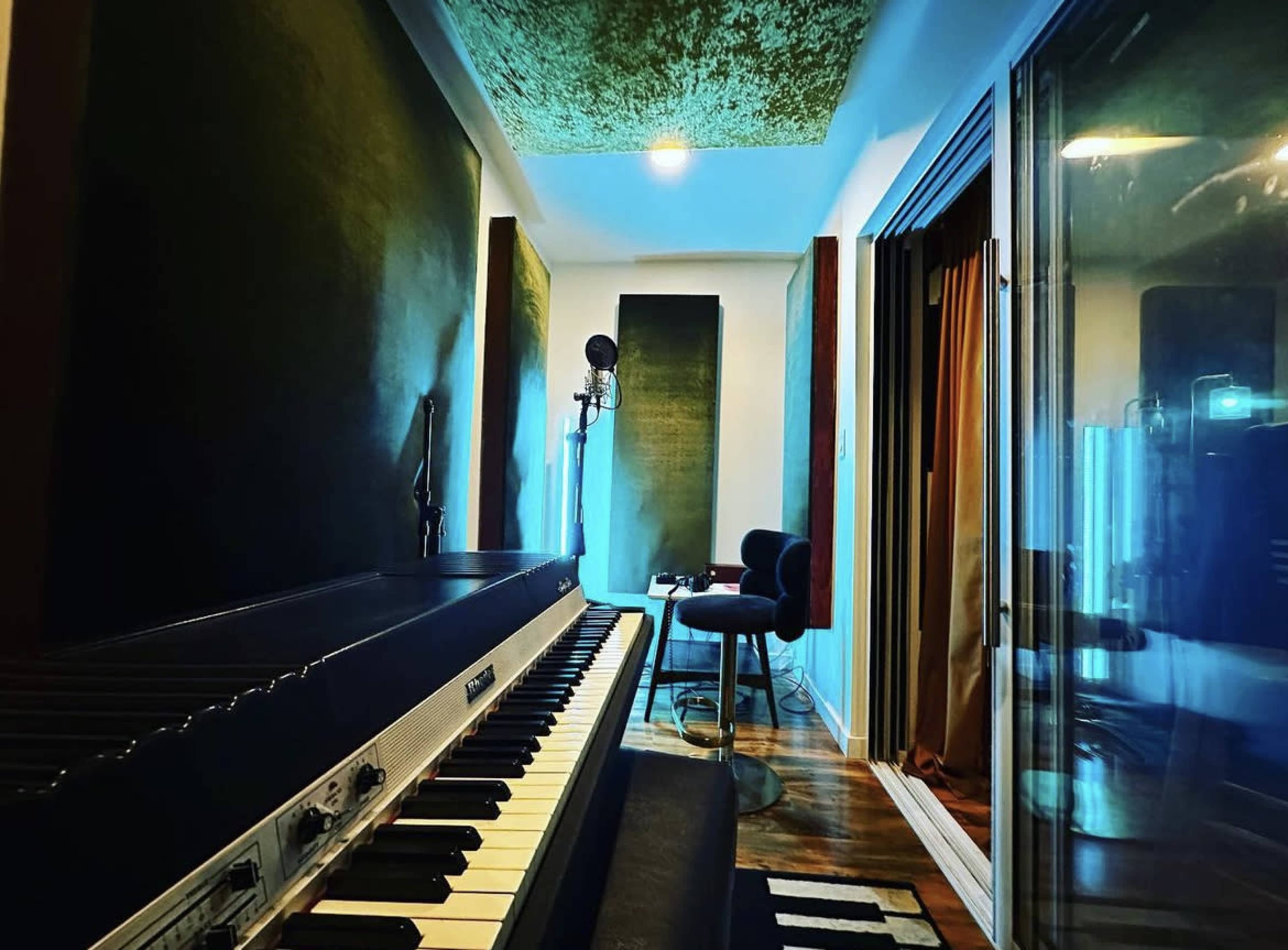 The image shows a music studio with a piano, microphone, and soundproof walls, illuminated by soft lighting.