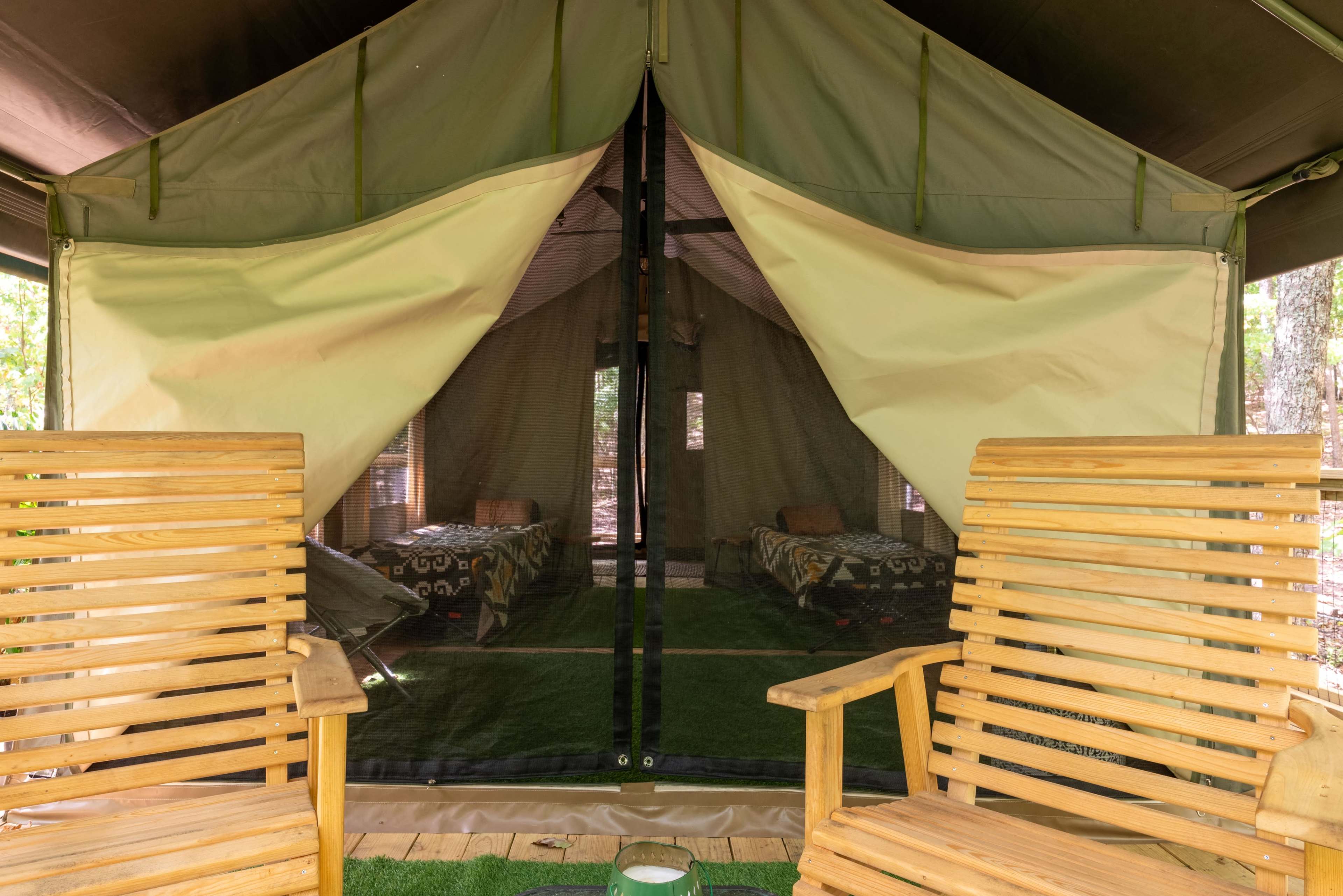 A spacious tent with two wooden chairs is set on a grassy area, revealing two neatly made beds inside.