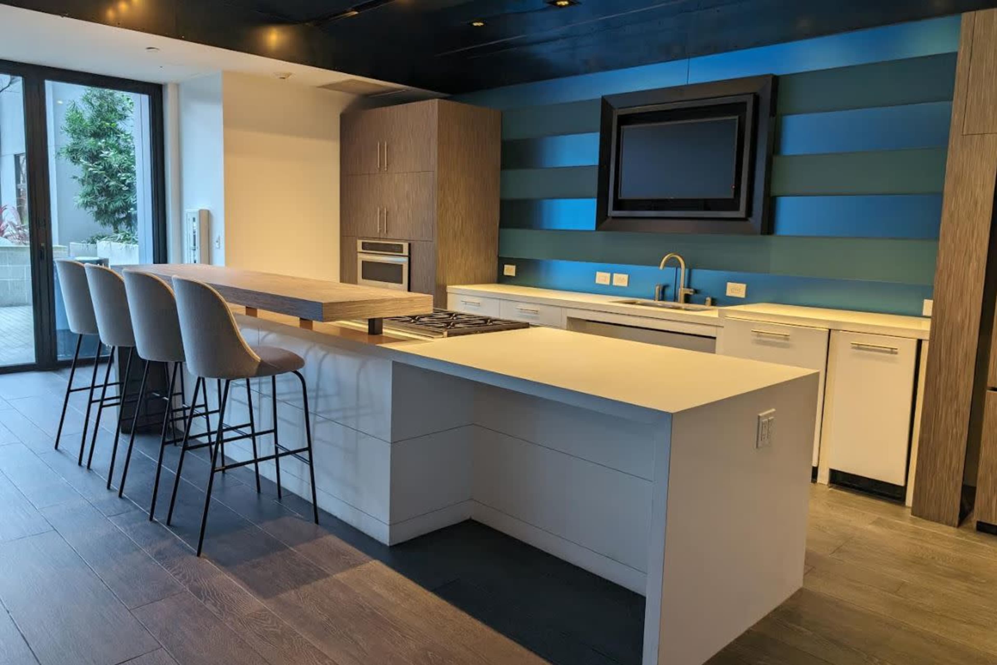A modern kitchen featuring a large island with barstools, sleek cabinetry, and a wall-mounted television.