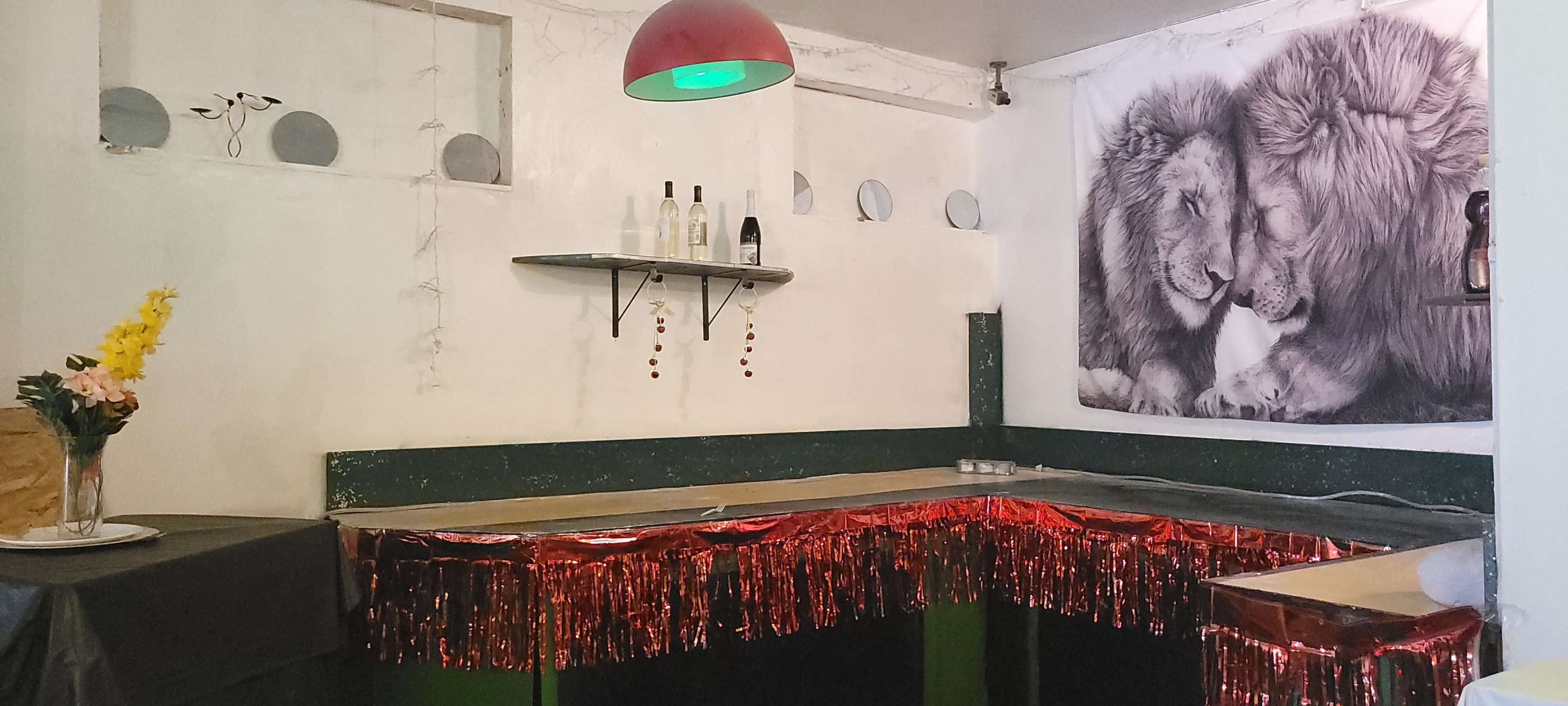 A bar area with a glittering red decoration along the counter, a shelf holding bottles, and a large black and white leopard photo on the wall.