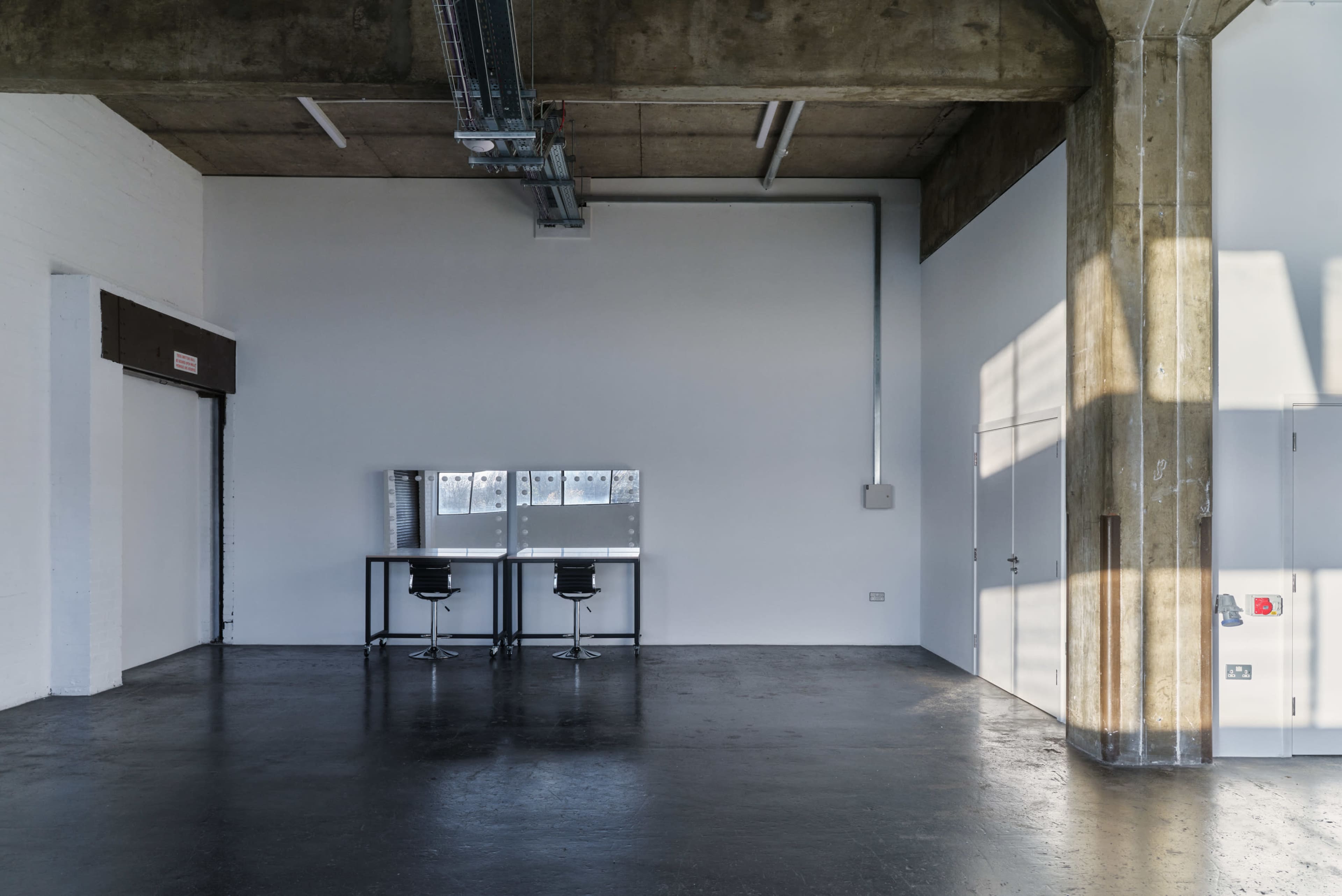 A minimalist, industrial-style room with two bar stools at a table against a stark, white wall.