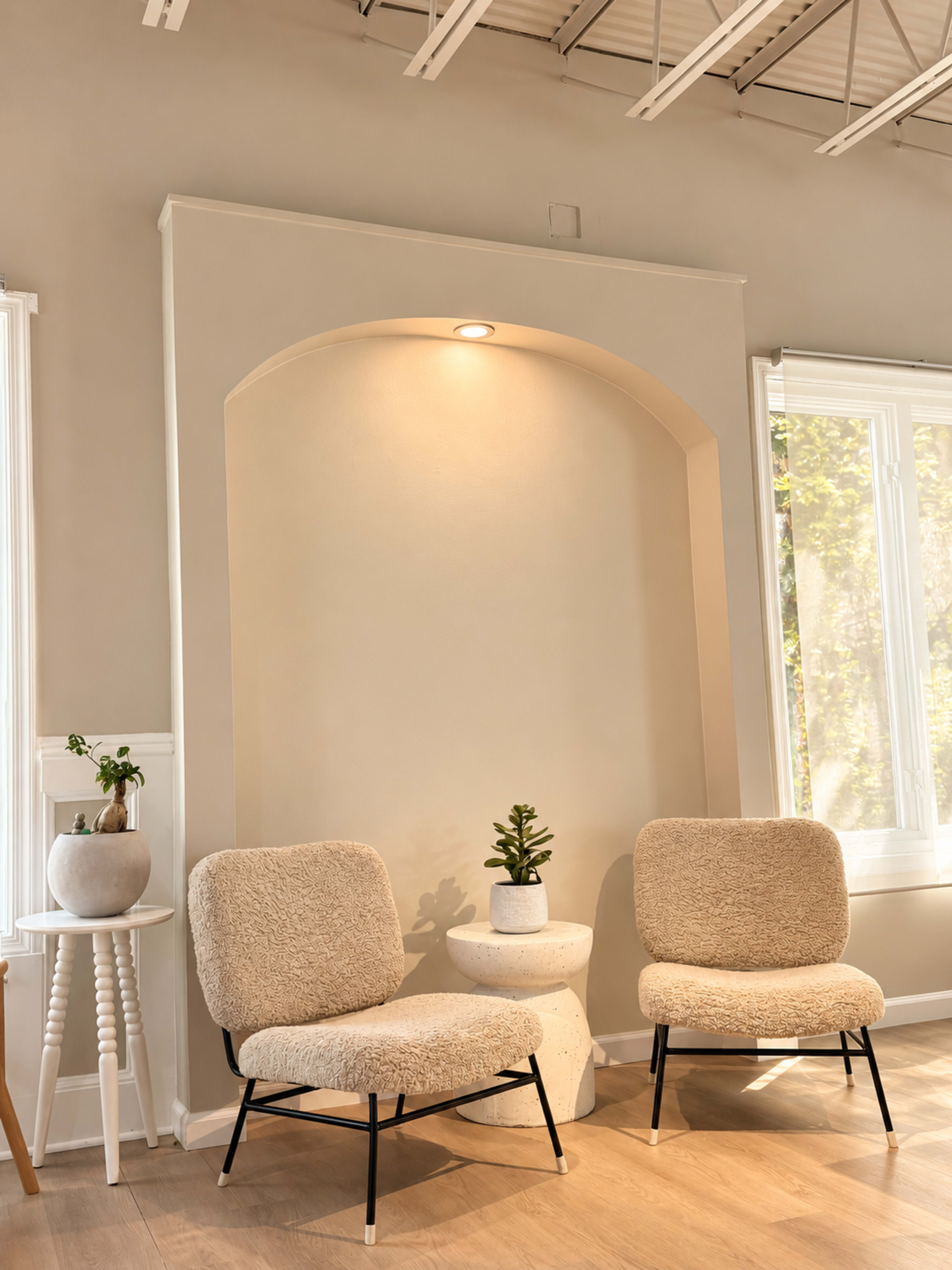 Two beige lounge chairs are positioned facing each other in a minimalist room with a softly lit alcove and a small plant on a pedestal table.