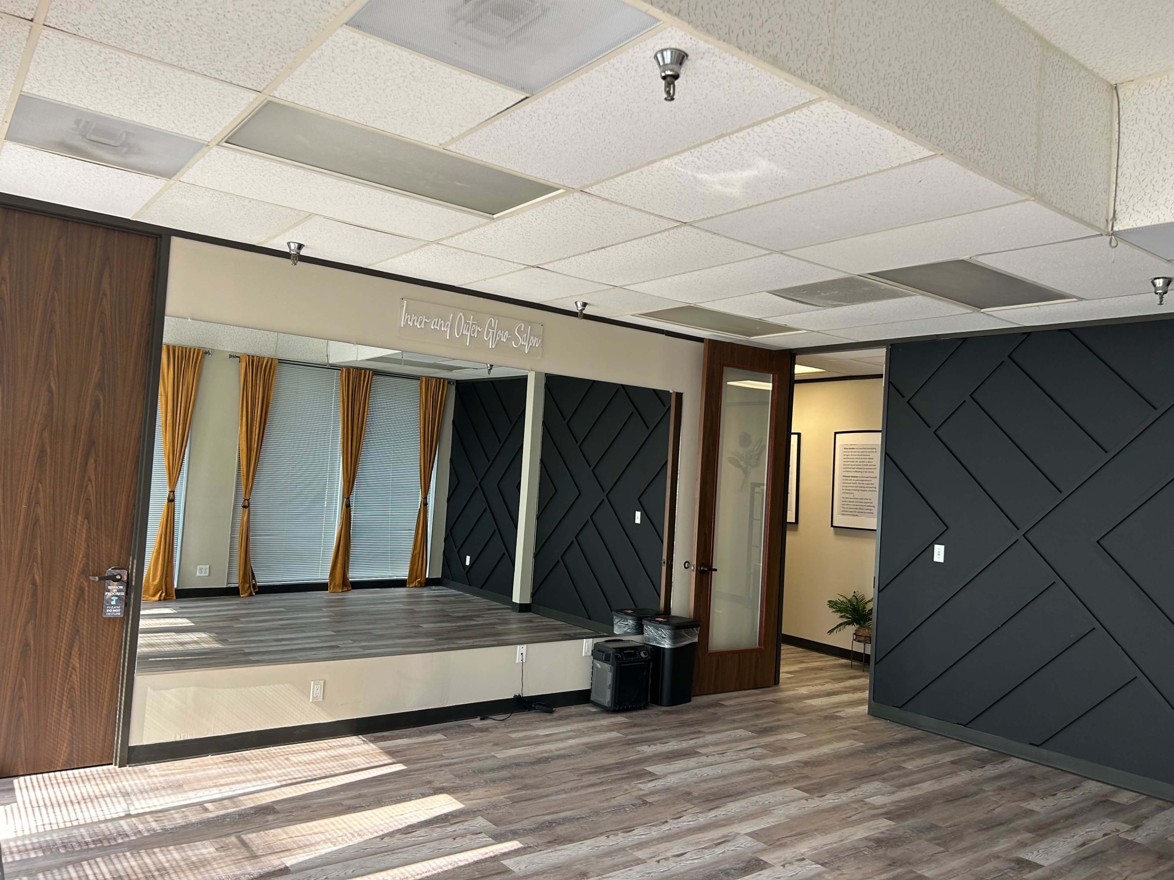 The image shows a well-lit room featuring a large mirror, decorative wall panels, and large windows with yellow curtains.