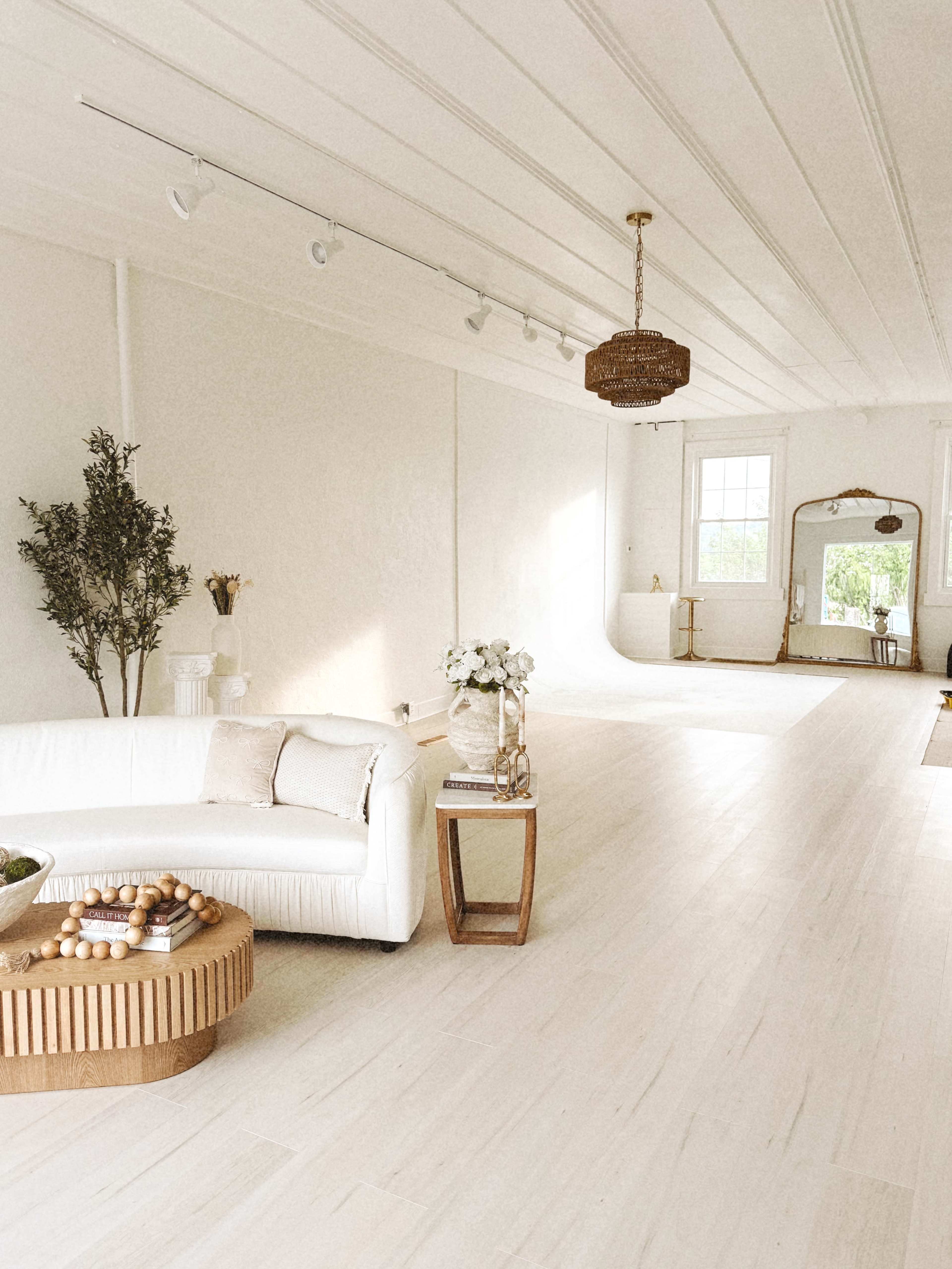 The image shows a bright, spacious room with white walls, a light-colored wooden floor, a white sofa, and a decorative table with a bowl of objects.