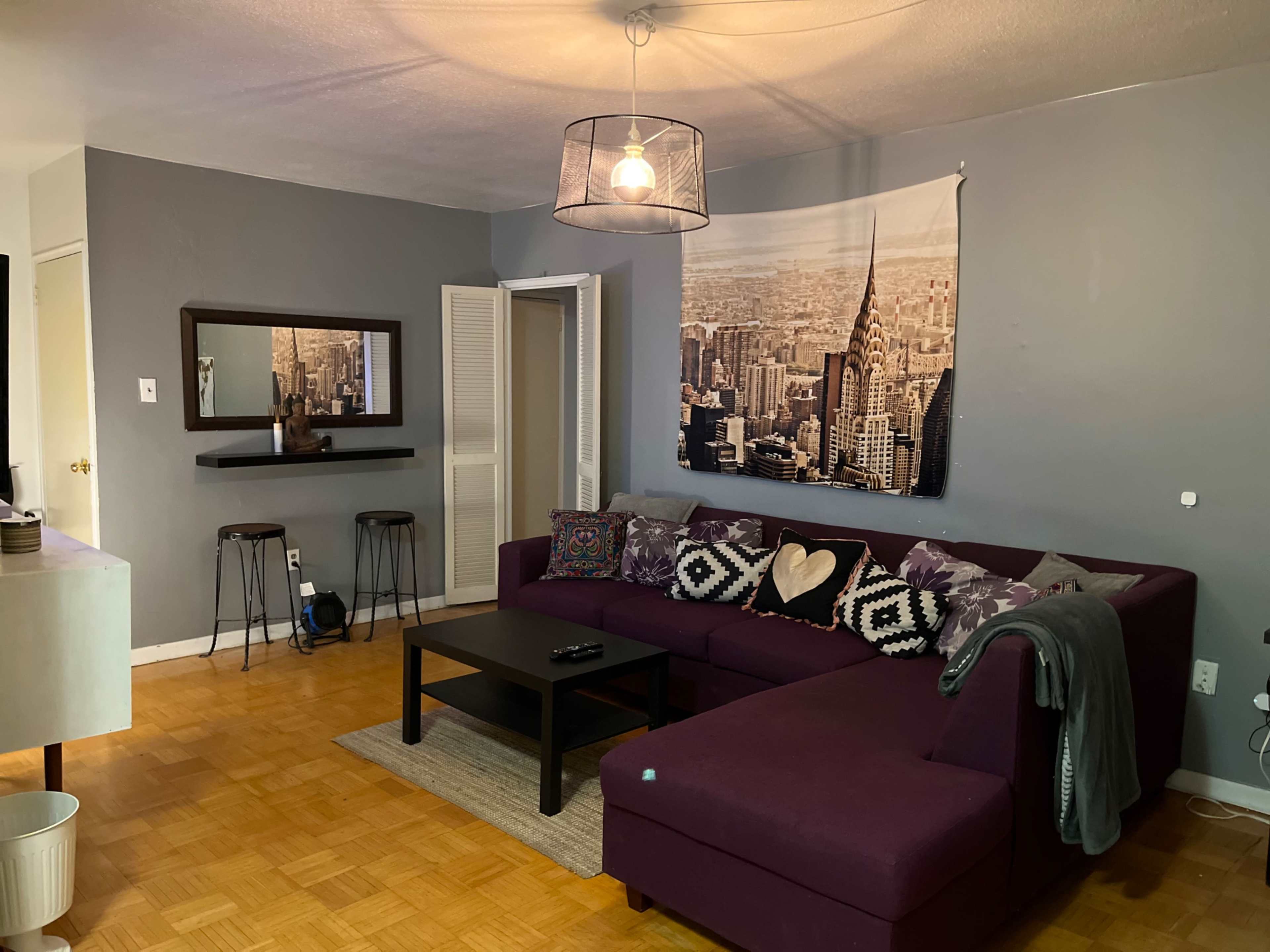 A living room with a purple sectional sofa, a coffee table, and a wall-mounted cityscape photograph.