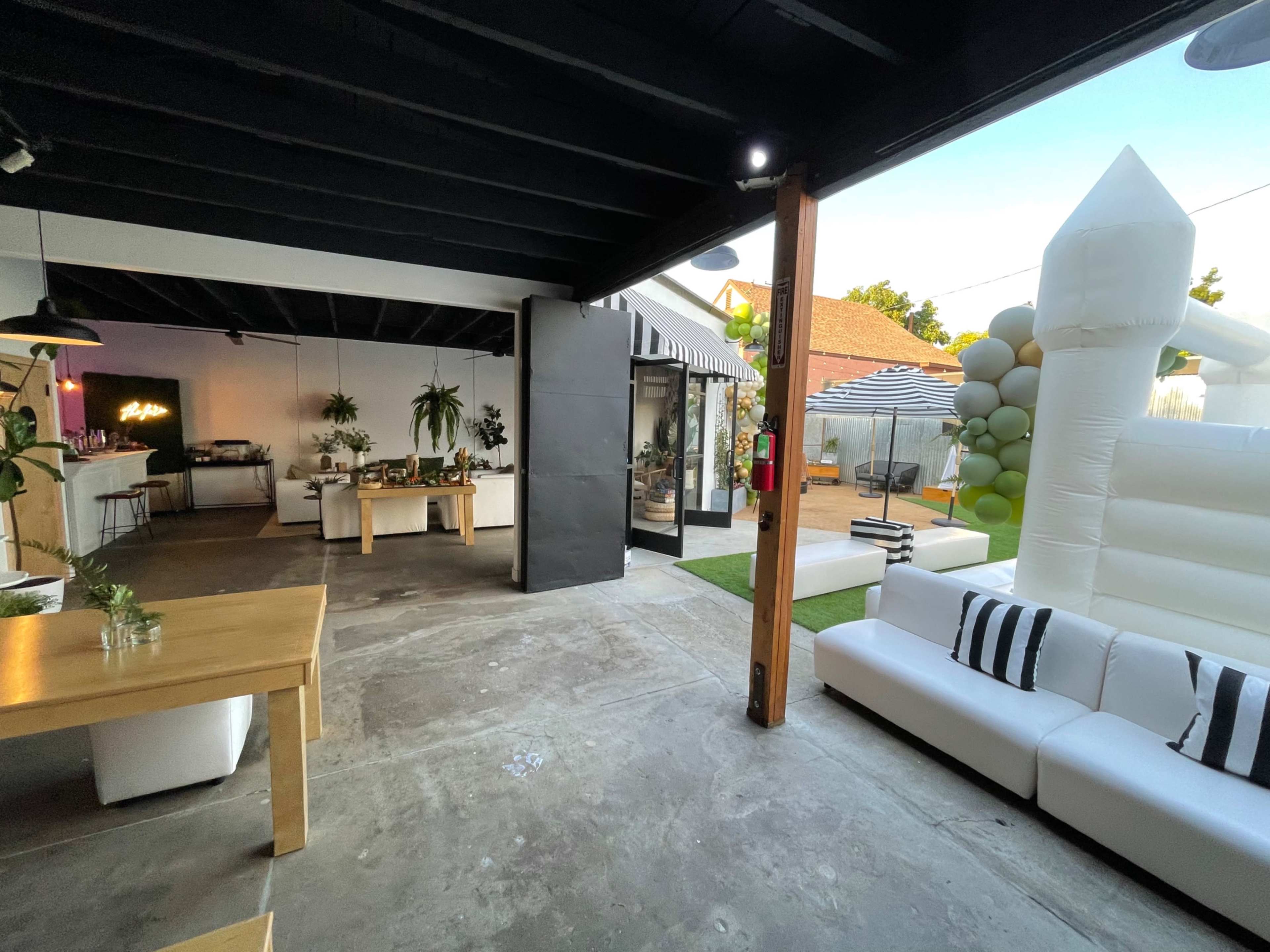 A spacious, modern indoor and outdoor area featuring a white sofa, a wooden table, and a large inflatable bounce house in the backyard.
