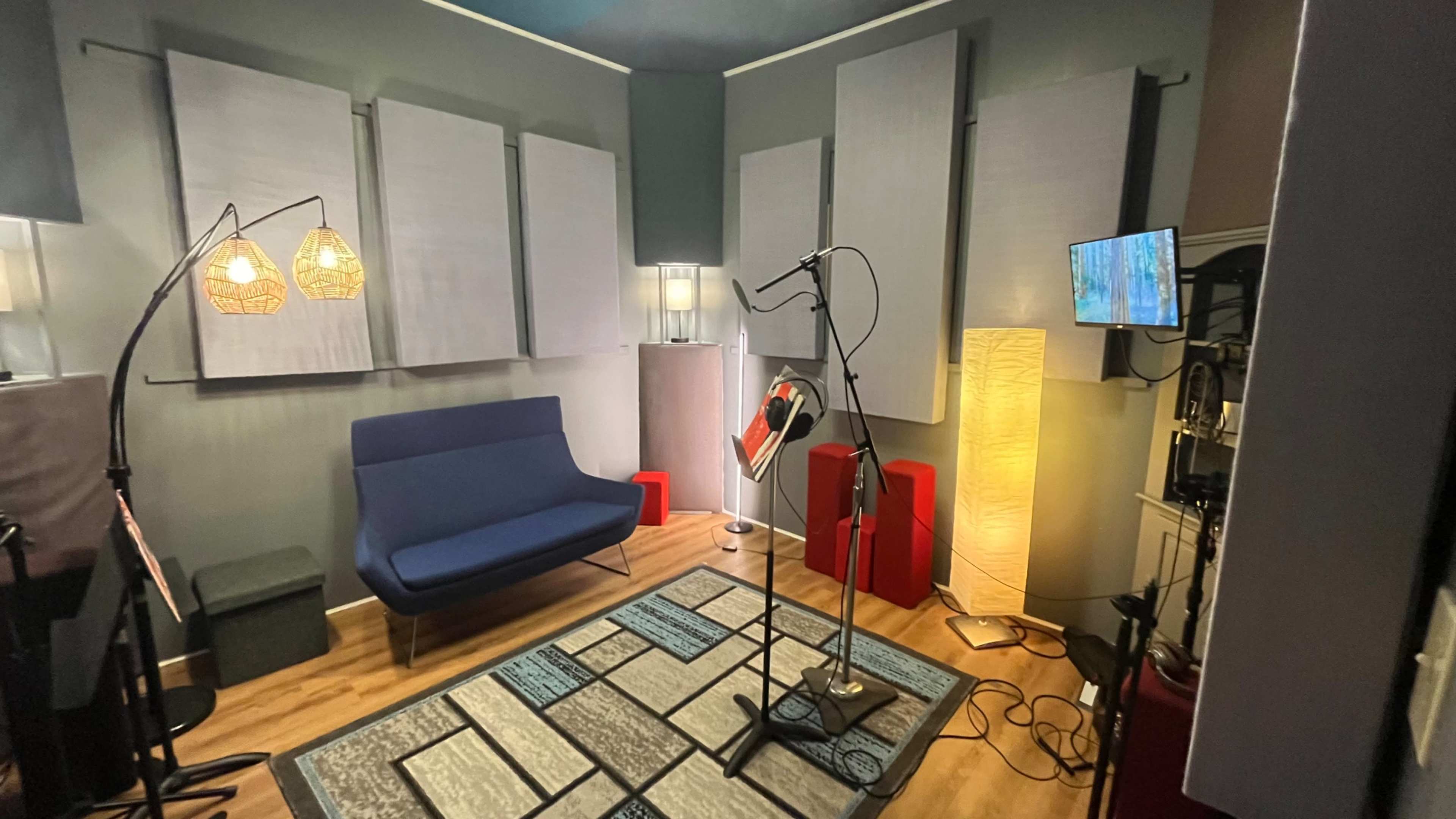 The image shows a soundproof recording studio with acoustic panels on the walls, a microphone stand, and various lighting sources.