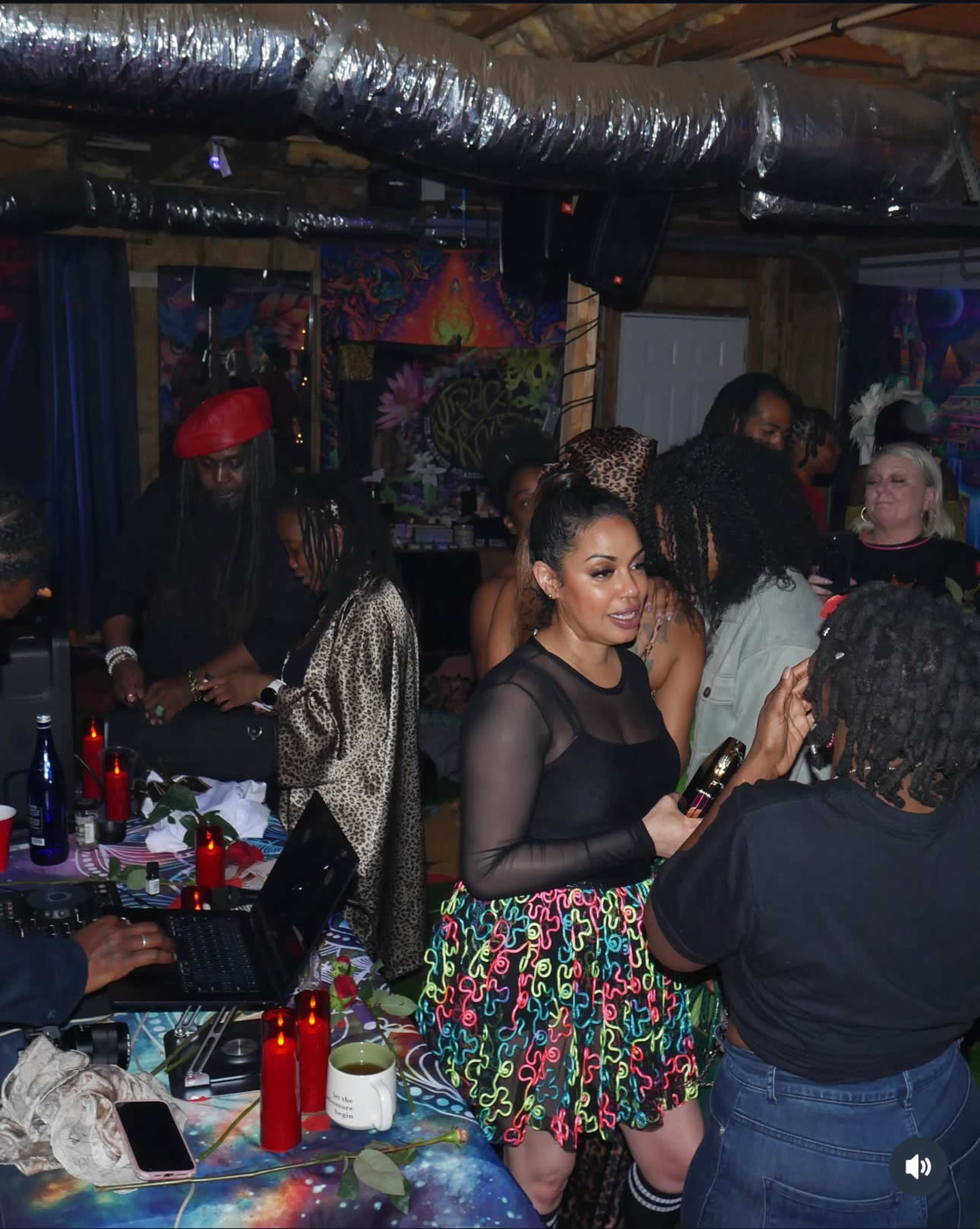 The image shows a vibrant party scene in a decorated basement, with people engaged in conversation and music playing.