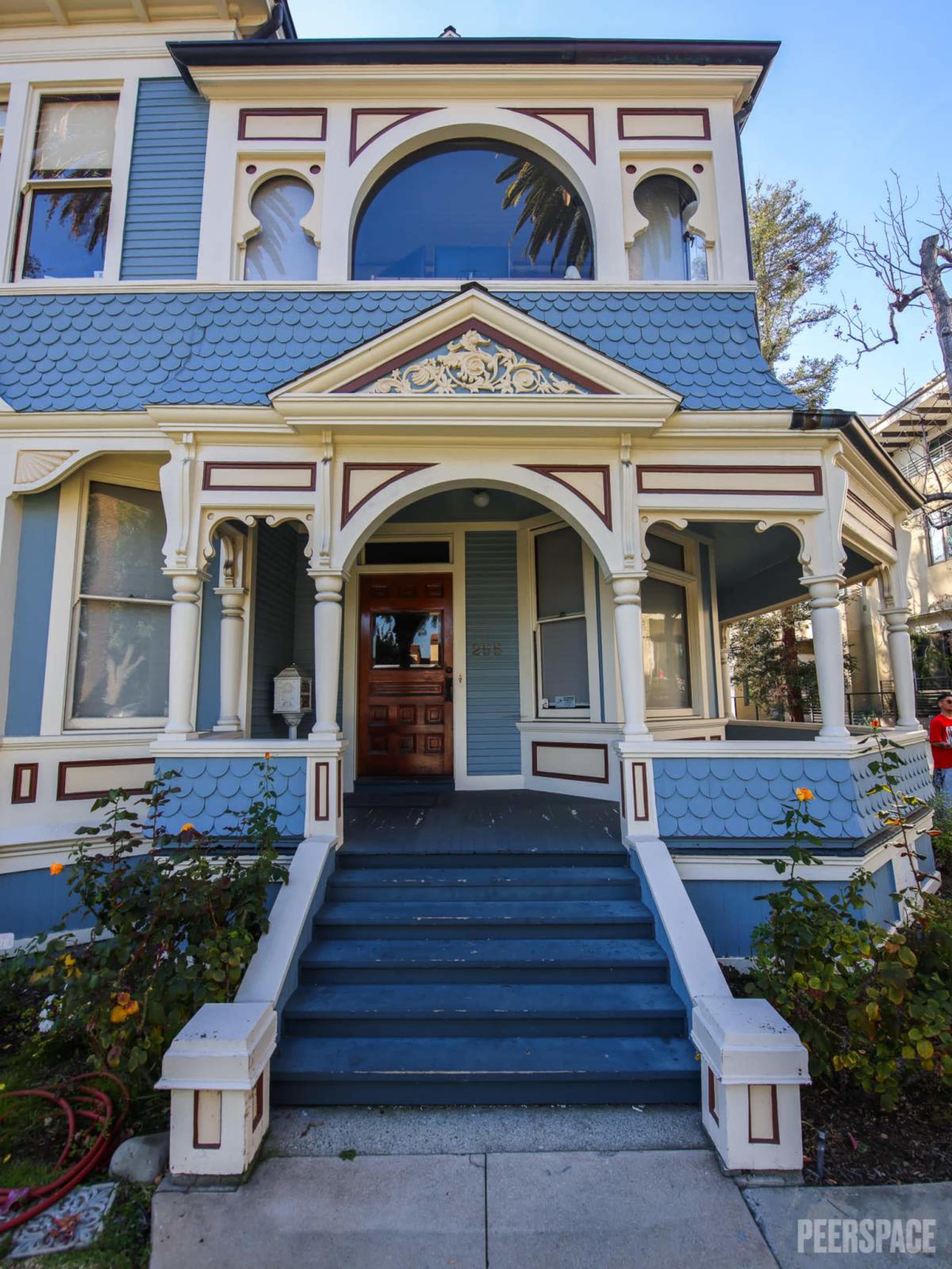 The image features a Victorian-style house with a blue exterior, ornate architectural details, and a prominent arched entrance.