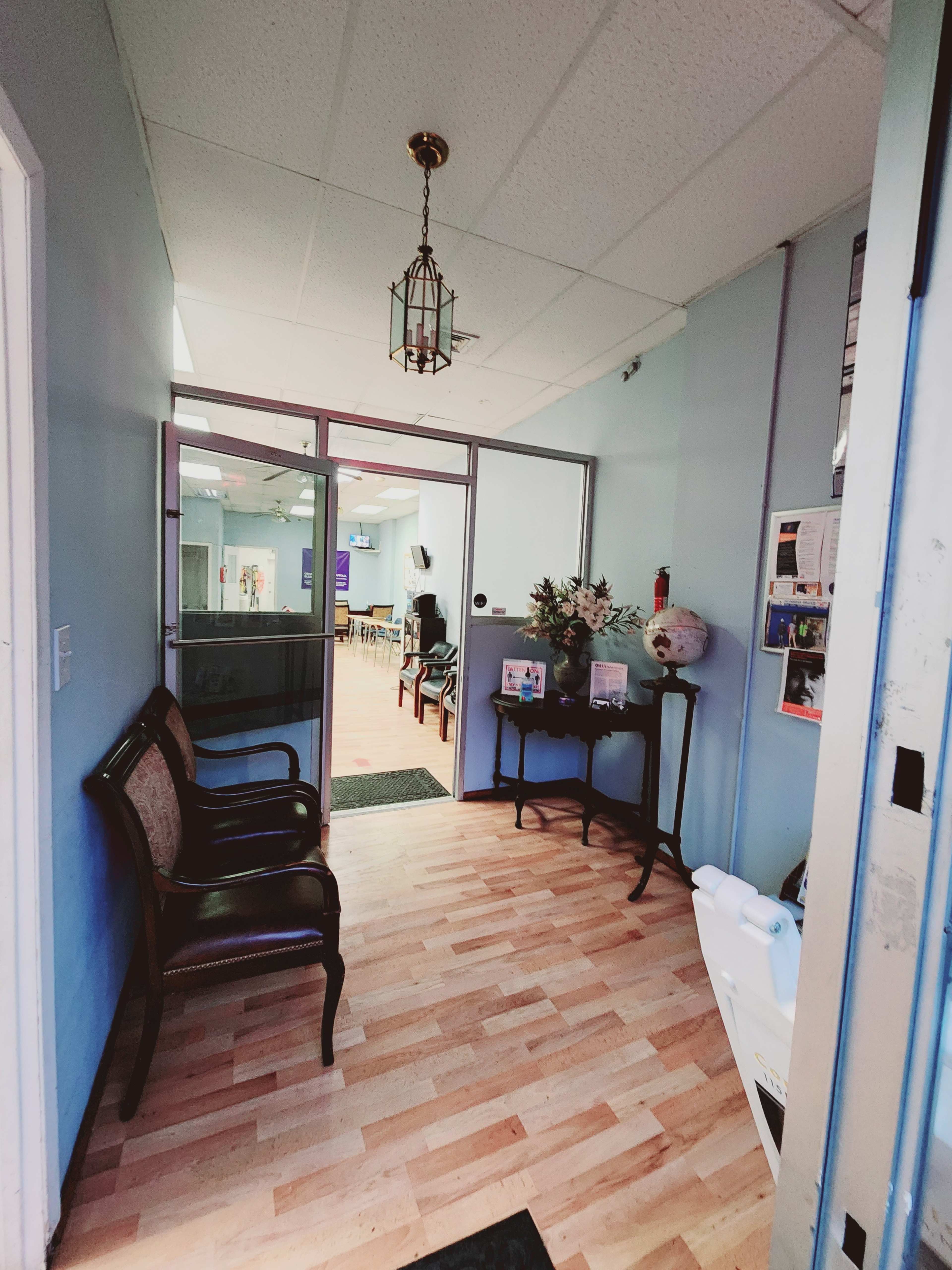 A hallway leading into a waiting area with a wooden floor, a bench, and framed photos on a table.